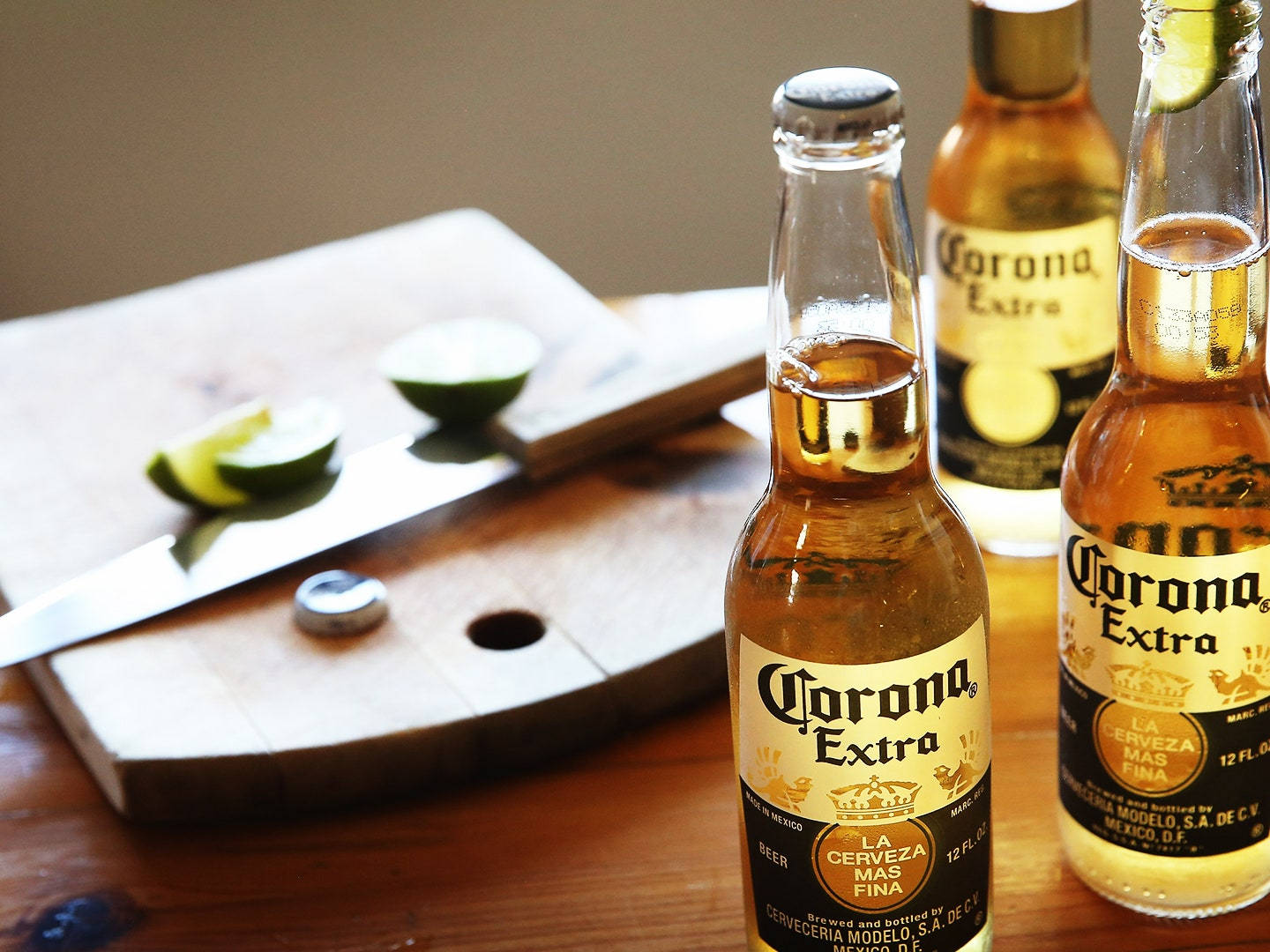 Corona Extra經典墨西哥飲品 壁紙 — 兩瓶Corona Extra啤酒連青檸角放在木桌上，旁邊有砧板、刀和半個青檸。