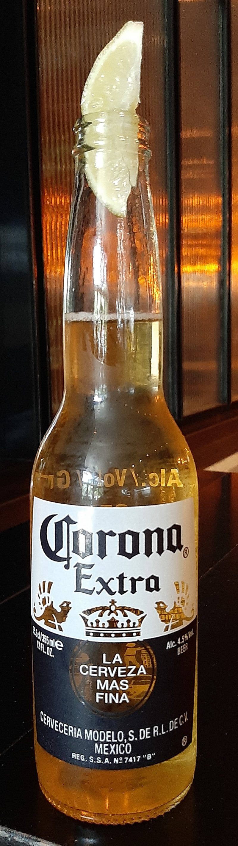 Corona Extra配檸檬 壁紙 — 一瓶冰凍的Corona Extra啤酒，瓶口放著一片青檸，在深色木質背景下溫暖地發光。
