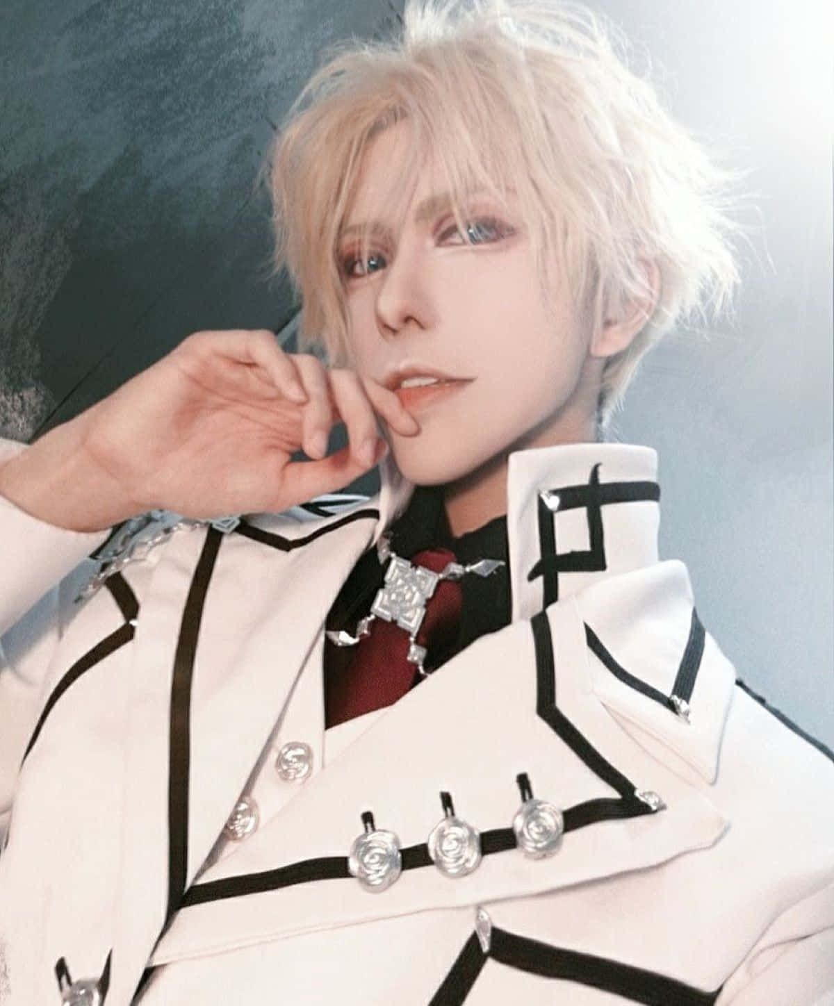  壁紙 — 一位擁有鉑金色頭髮和藍眼睛的角色扮演者，穿著帶有銀色鈕扣和紅色領帶的詳細黑白制服，背景為柔和的灰色。