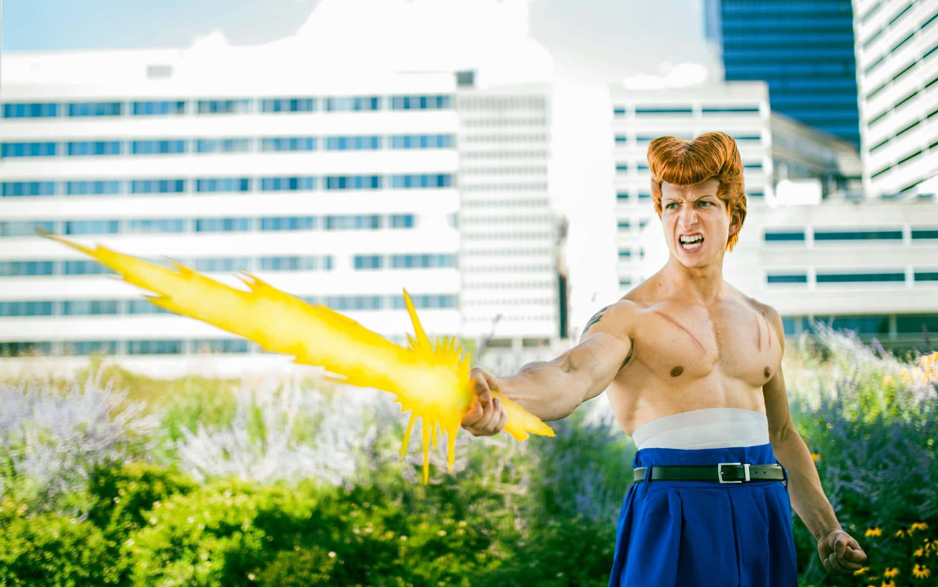  壁紙 — 一位扮演超級英雄的cosplayer，發出熾熱的黃色能量爆炸，站在長滿草的城市屋頂上，背景是現代建築。