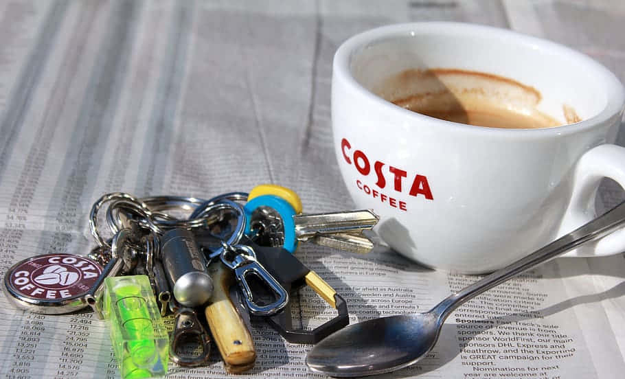 Costa咖啡杯與茶匙 壁紙 — 一個Costa Coffee杯和鑰匙放在報紙上，附近有一隻匙羹。
