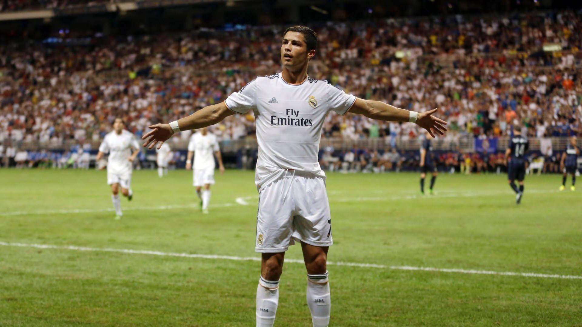 CR7 全白球衣 壁紙 — 一名身穿白色皇家馬德里球衣的足球運動員在燈光明亮的球場上張開雙臂站立，背景中球迷們在歡呼。
