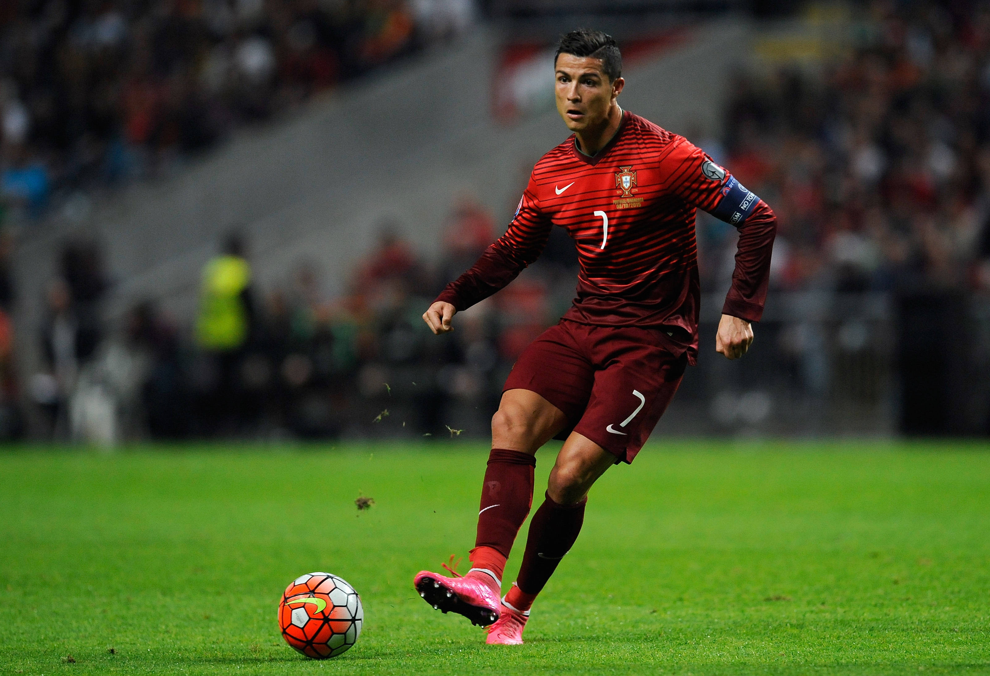 CR7 紅色球衣 壁紙 — 基斯坦奴·朗拿度身穿紅色葡萄牙球衣，在球場燈光下於充滿活力的綠色場地上盤球。