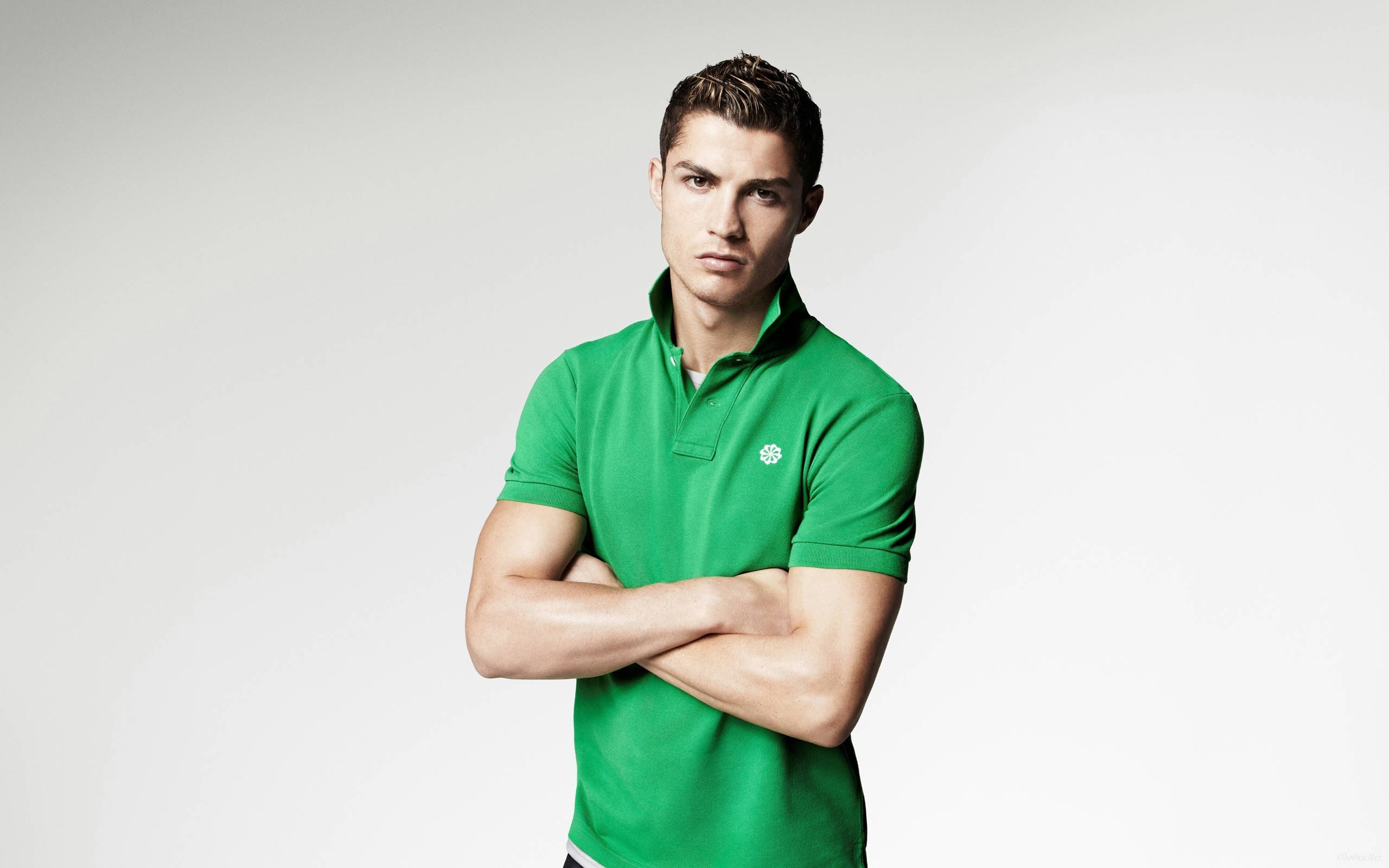 CR7 綠色Polo衫 壁紙 — 一個肌肉發達的男人穿著亮綠色Polo衫，雙手交叉，自信地站在純白色背景前。