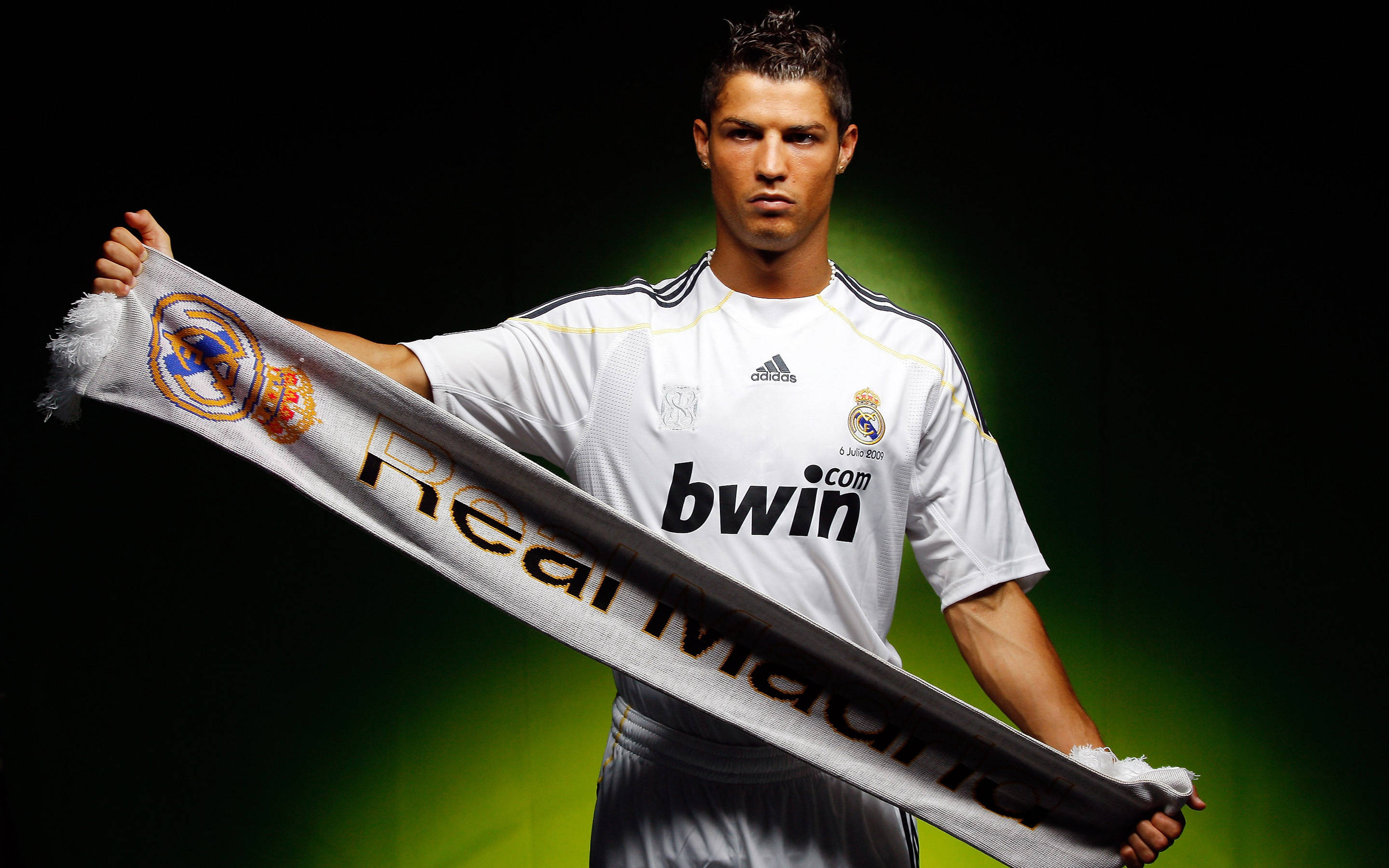 CR7 與皇家馬德里橫幅 壁紙 — 一名身穿白色皇家馬德里球衣的足球員，在帶有綠色燈光的深色背景前舉起球隊圍巾。