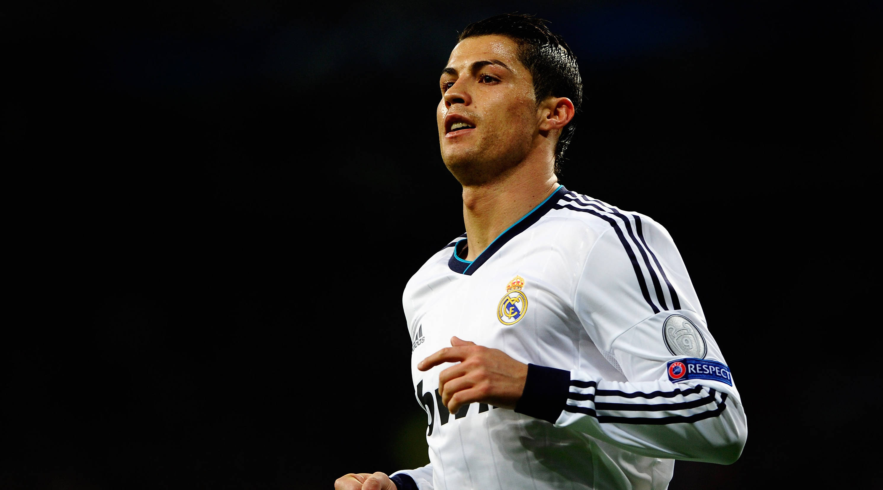 CR7 英超聯賽 壁紙 — 一位專注的足球員身穿白色皇家馬德里球衣，在球場燈光下以黑暗背景奔跑。