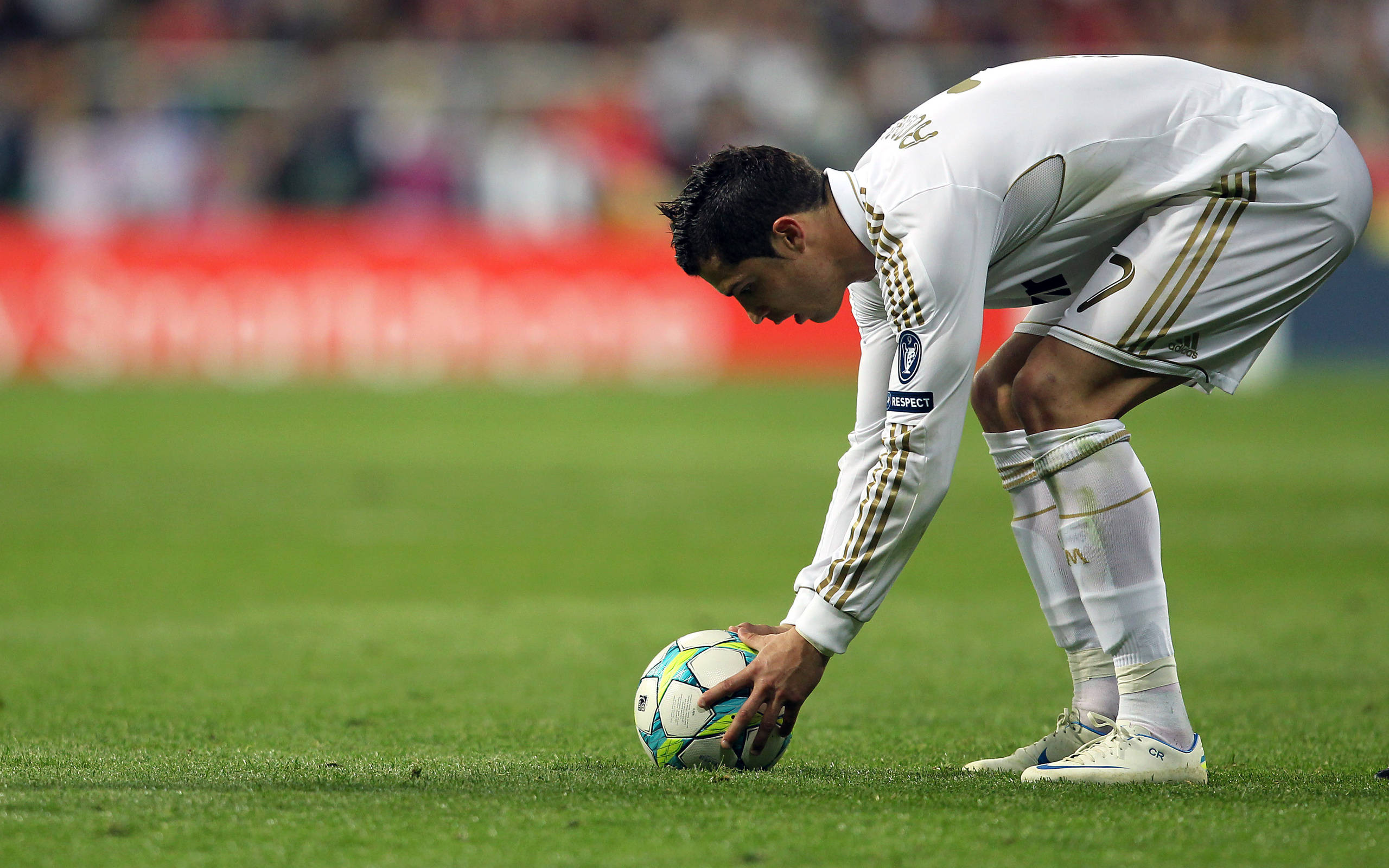 CR7 足球球 壁紙 — 一名身穿白色球衣的足球員在體育場燈光下，在充滿活力的綠色球場上彎腰觸碰一個色彩繽紛的足球。