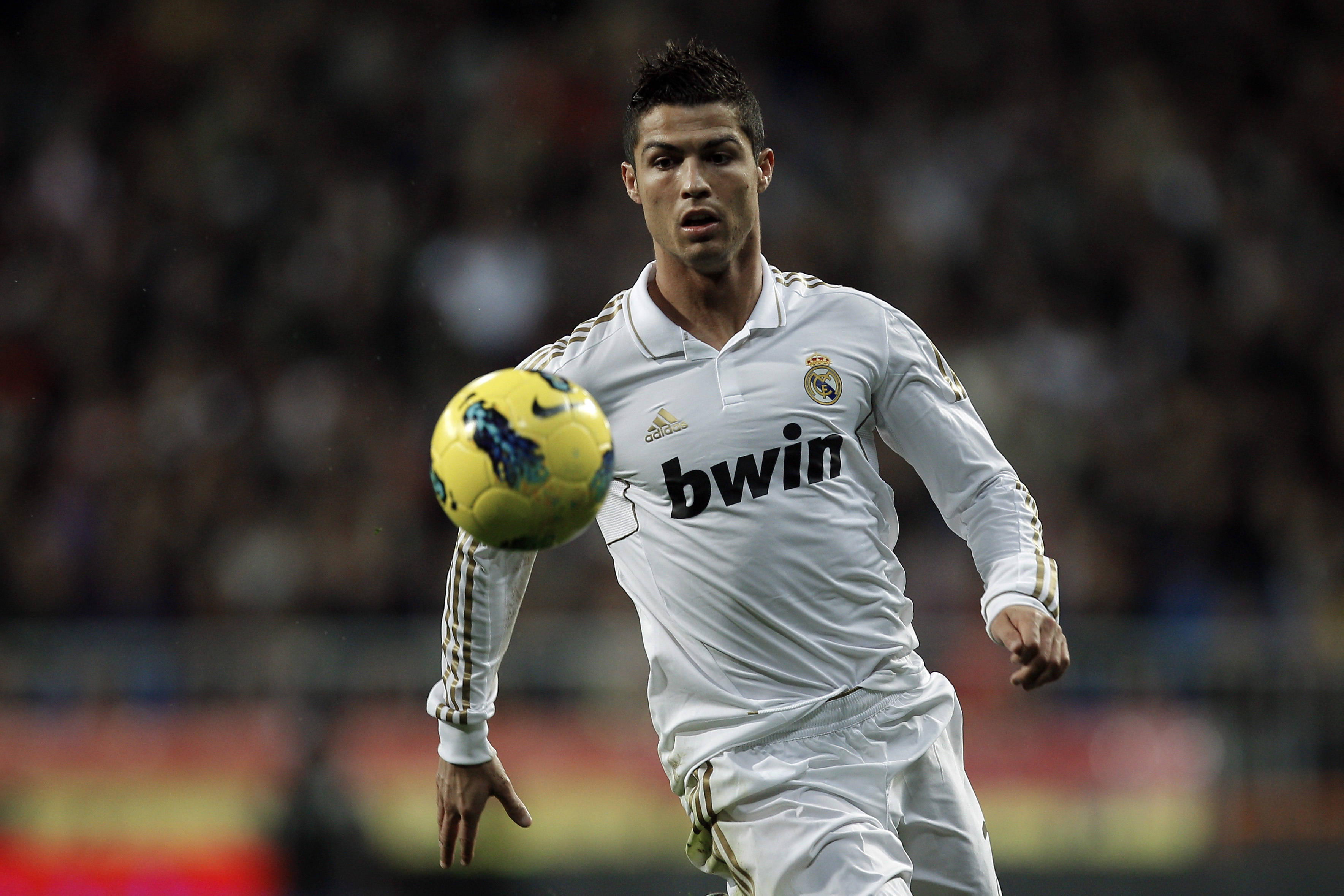 CR7 追逐黃色足球 壁紙 — 一名專注的足球員身穿白色皇家馬德里球衣，在夜間比賽中於球場燈光下盤帶黃色足球。