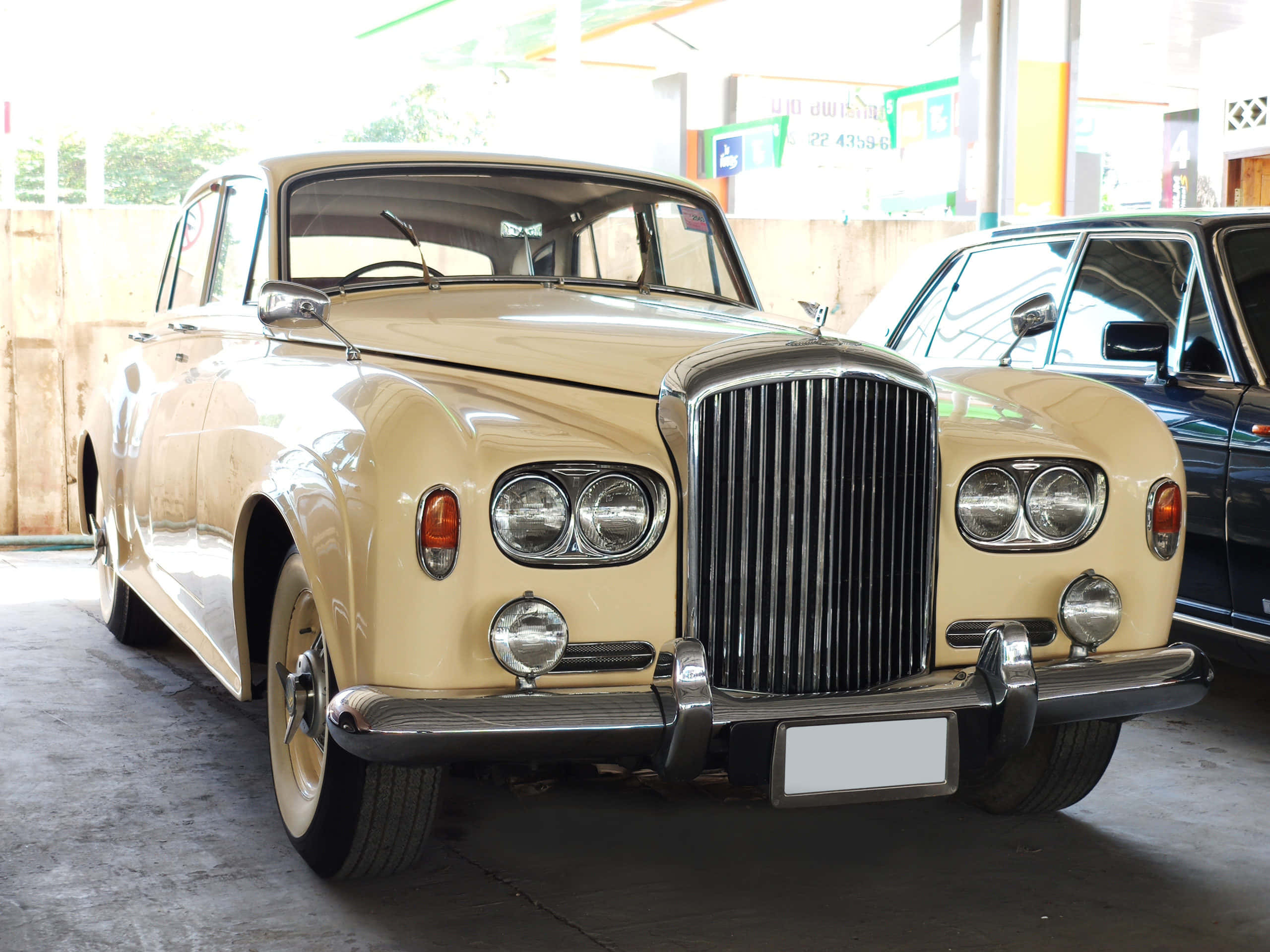 Bentley S3 桌布 壁紙 — 一輛奶油色經典賓利，帶有鍍鉻格柵和圓形頭燈，停在加油站明亮的遮陽篷下。
