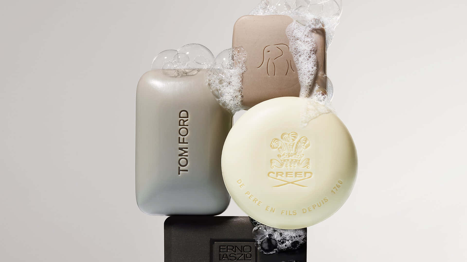 Creed 香皂 壁紙 — 三塊來自Tom Ford Creed和Erno Laszlo的奢華肥皂，在簡約白色背景上漂浮著豐富的泡沫。