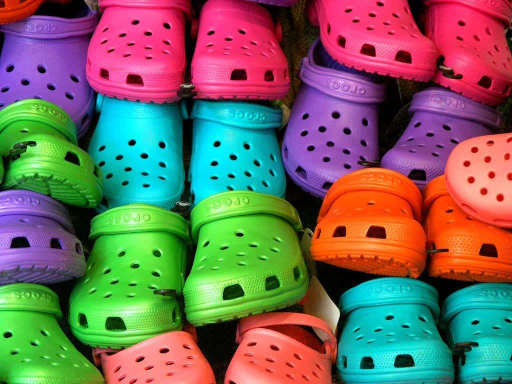 穿著Crocs，時尚又舒適地出街 壁紙 — 色彩繽紛的Crocs木屐堆疊成密集、引人注目的霓虹色調展示。