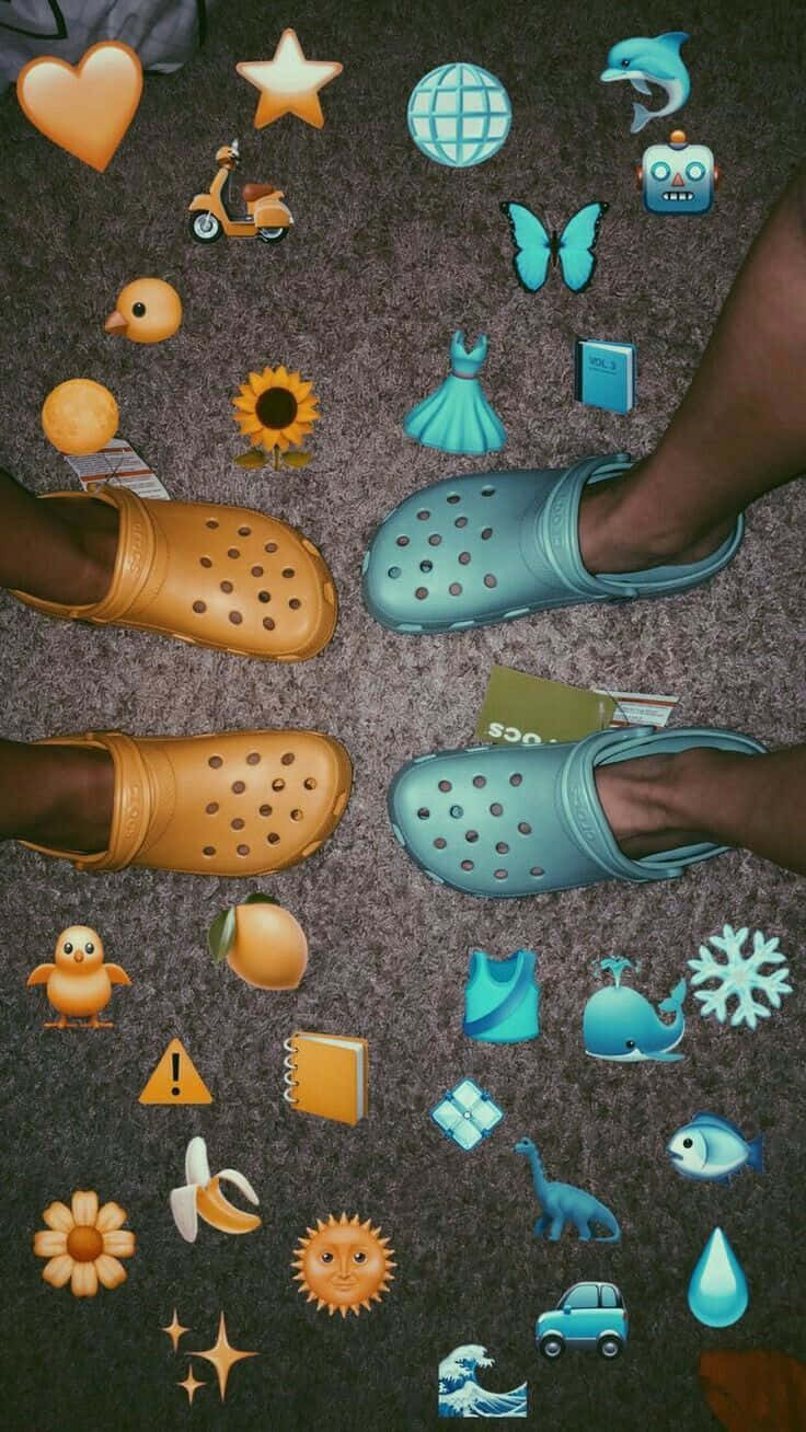 一雙經典的Crocs鞋，呈現其標誌性的深藍色調 壁紙 — 兩對色彩繽紛的Crocs鞋放在地毯上，周圍散落著表情符號貼紙。