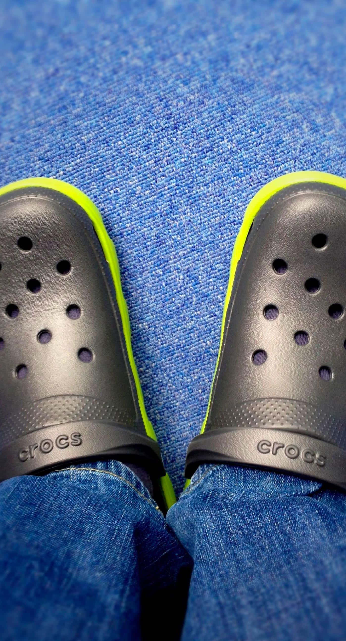 這個夏天，穿著Crocs放鬆自在 壁紙 — 黑色Crocs配螢光黃飾邊的特寫，放在有紋理的藍色地毯上。