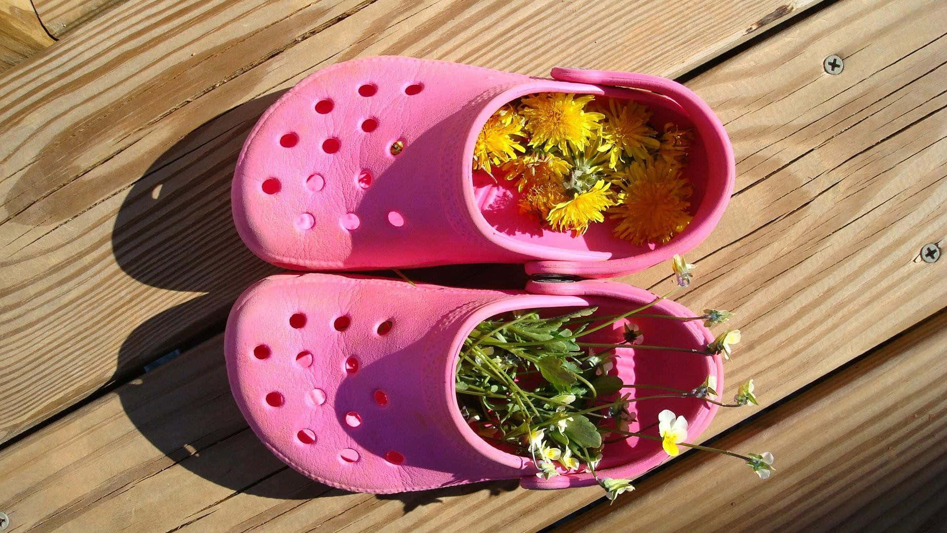 Crocs鞋履：風格與舒適的完美結合 壁紙 — 鮮粉紅色木屐裝滿黃色蒲公英和白色花朵，放在陽光普照的木甲板上。