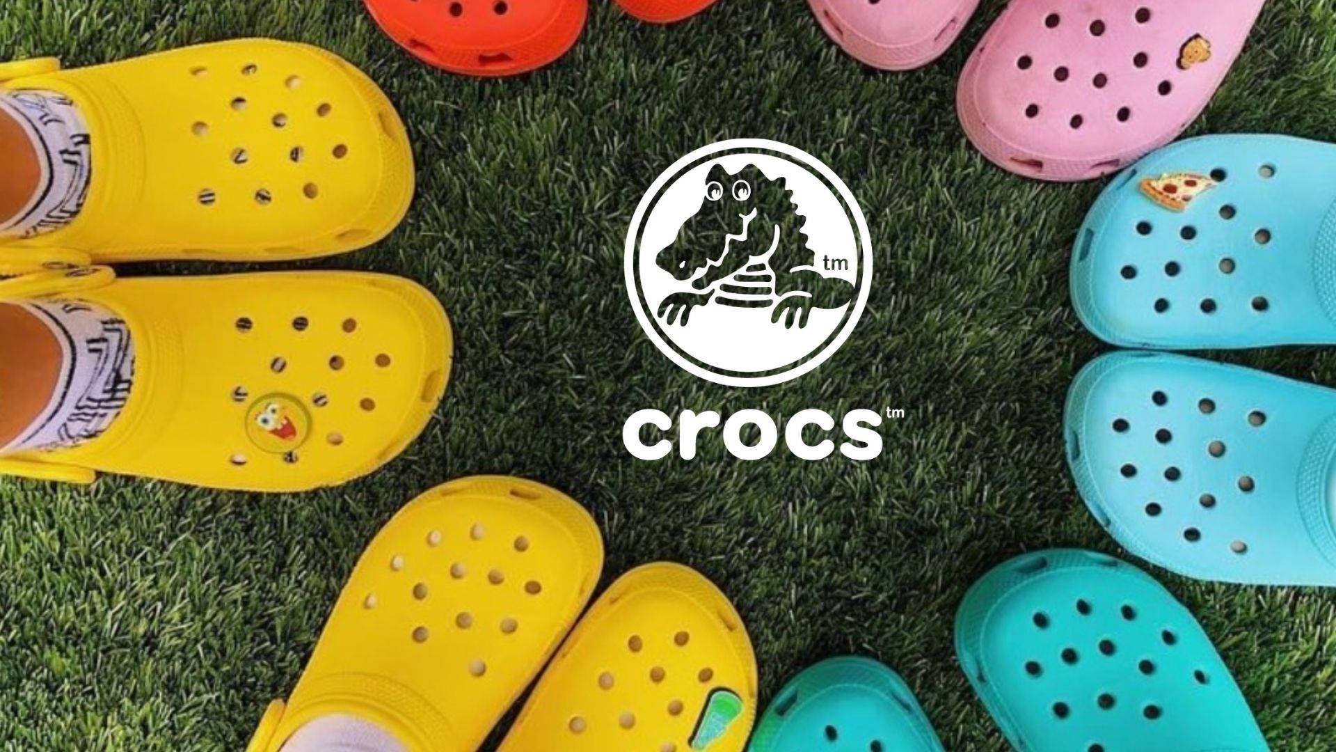 Crocs鞋款海報 壁紙 — 色彩繽紛的Crocs涼鞋在綠色草地上圍繞Crocs標誌排列成圓圈。