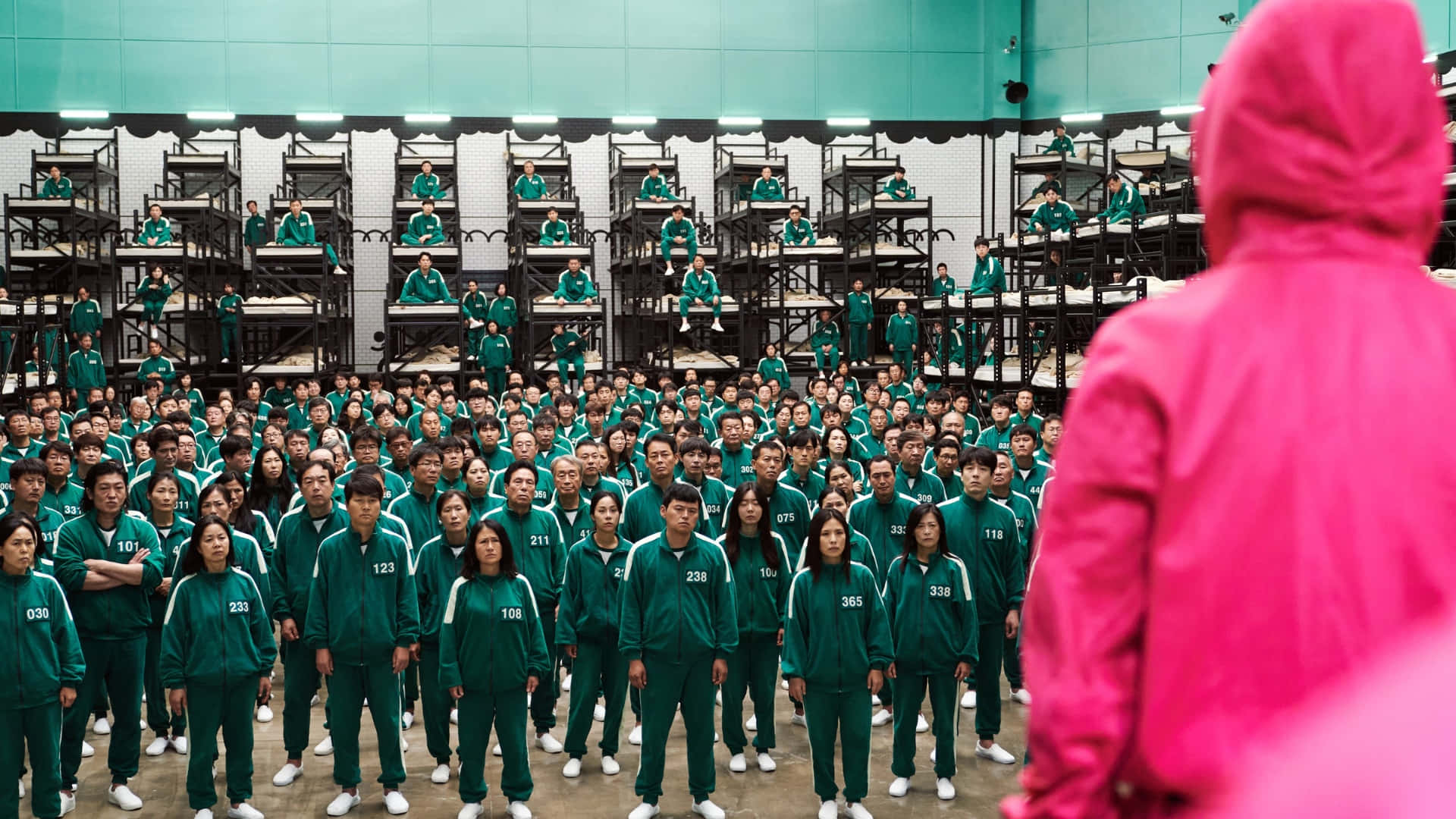  壁紙 — 一群穿著綠色運動服的人站在寬闊的工業房間裡，面對一個粉紅色連帽人物。