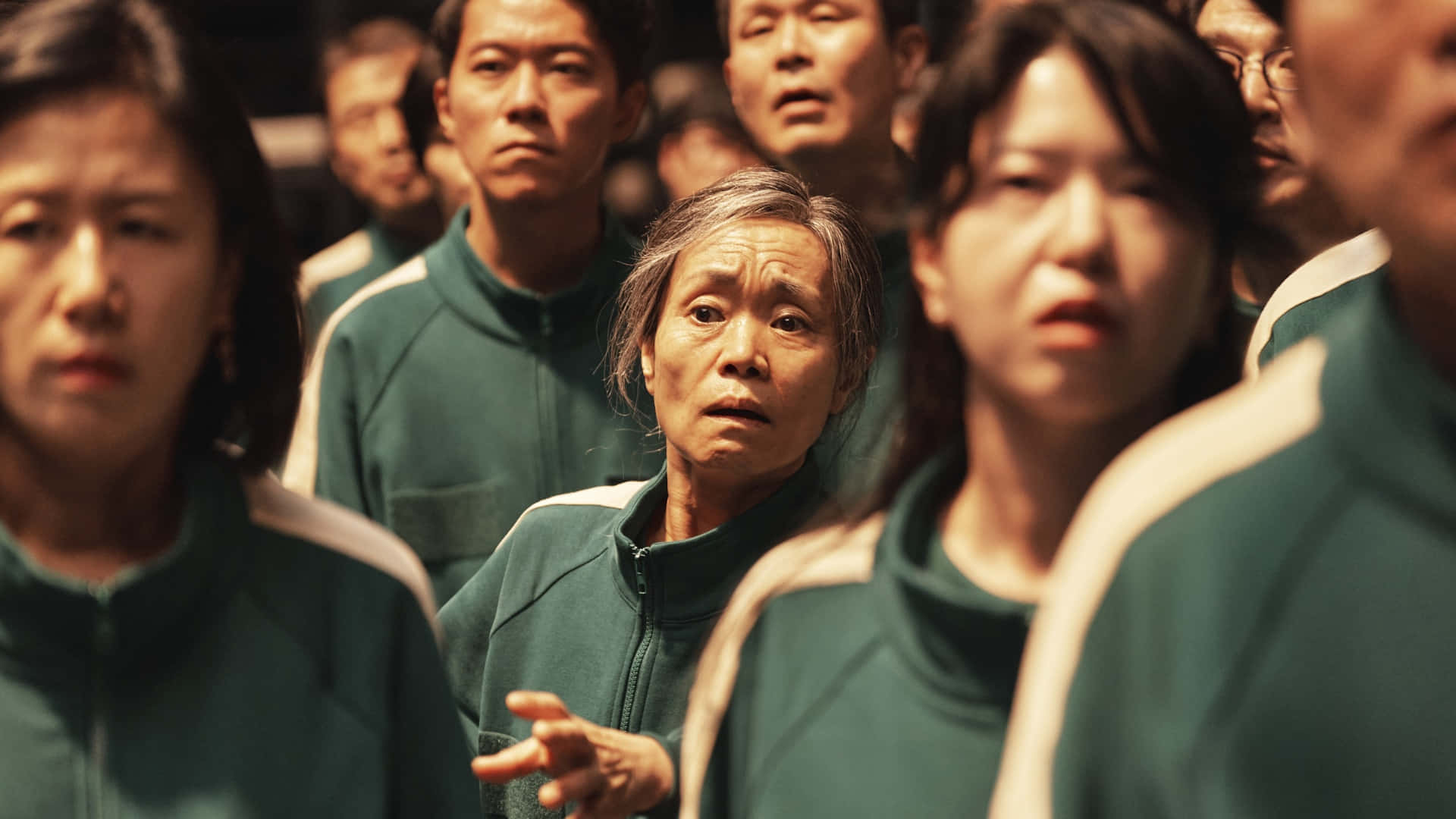  壁紙 — 一群穿著綠色運動服的人，帶著震驚和緊張的表情，專注地向前凝視。