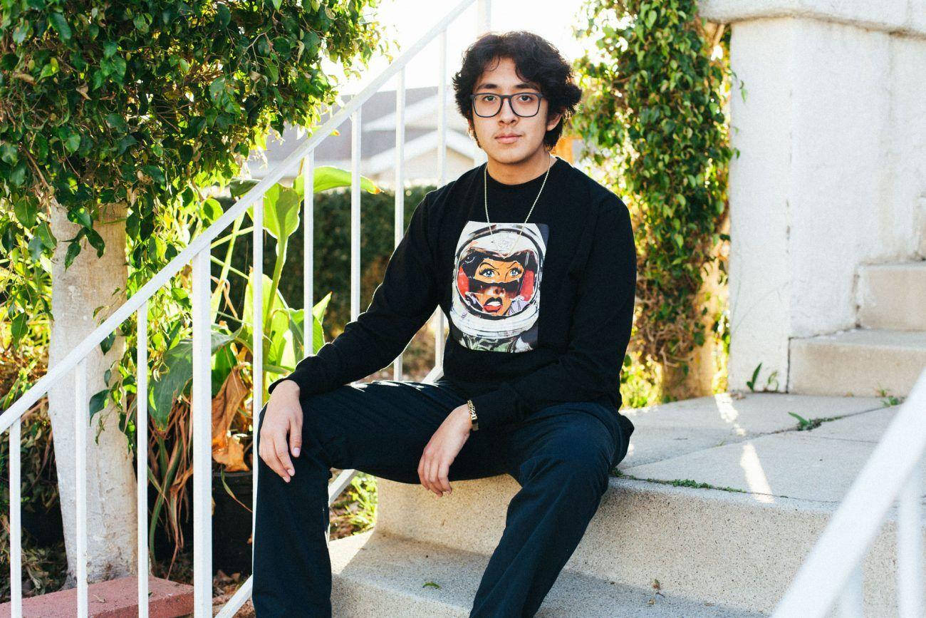 戴眼鏡的年輕男子坐在被綠植環繞的戶外台階上。