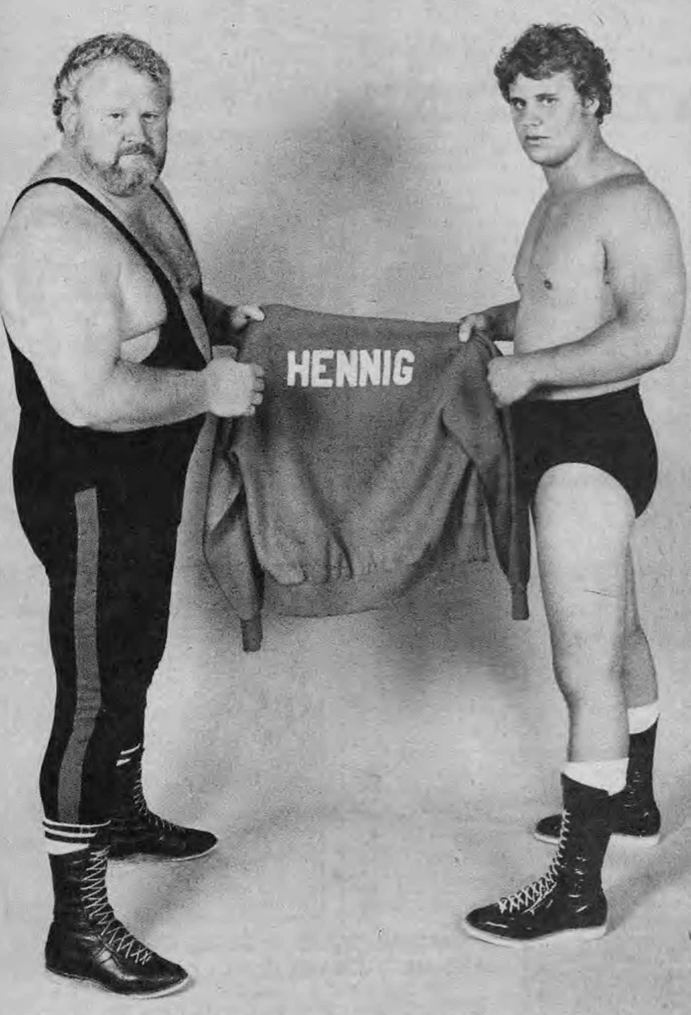 Curt Hennig 與 Larry Hennig 壁紙 — 兩名穿著復古裝備的肌肉摔角手在純色工作室背景前舉起一件印有「HENNIG」的外套。