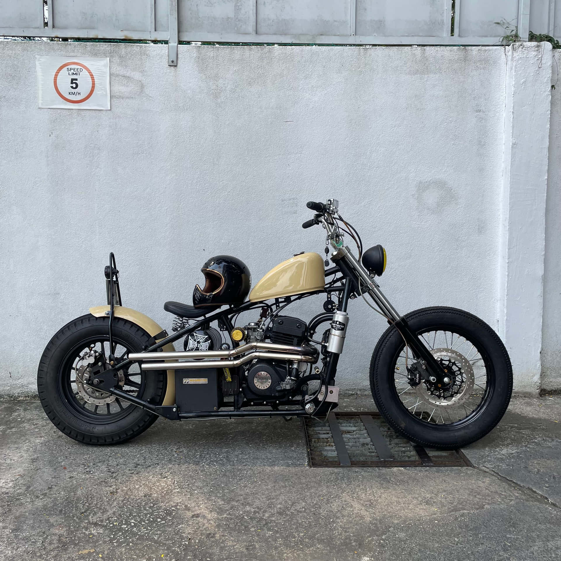  壁紙 — 一架自訂嘅chopper電單車，奶油色油缸同黑色頭盔，日頭泊喺白色牆邊。