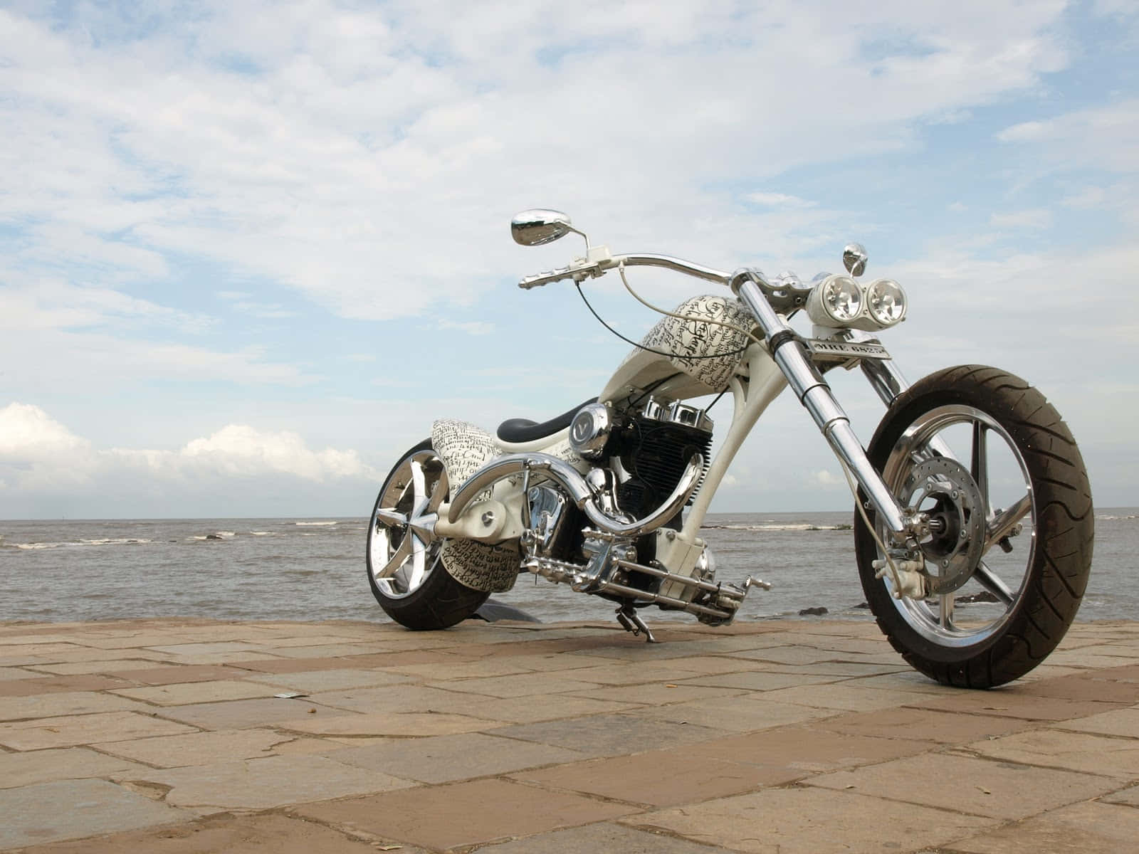 Vardenchi 桌布 壁紙 — 一架訂製白色chopper電單車帶有鍍鉻裝飾，站在石碼頭上，俯瞰海洋，天空部分多雲。