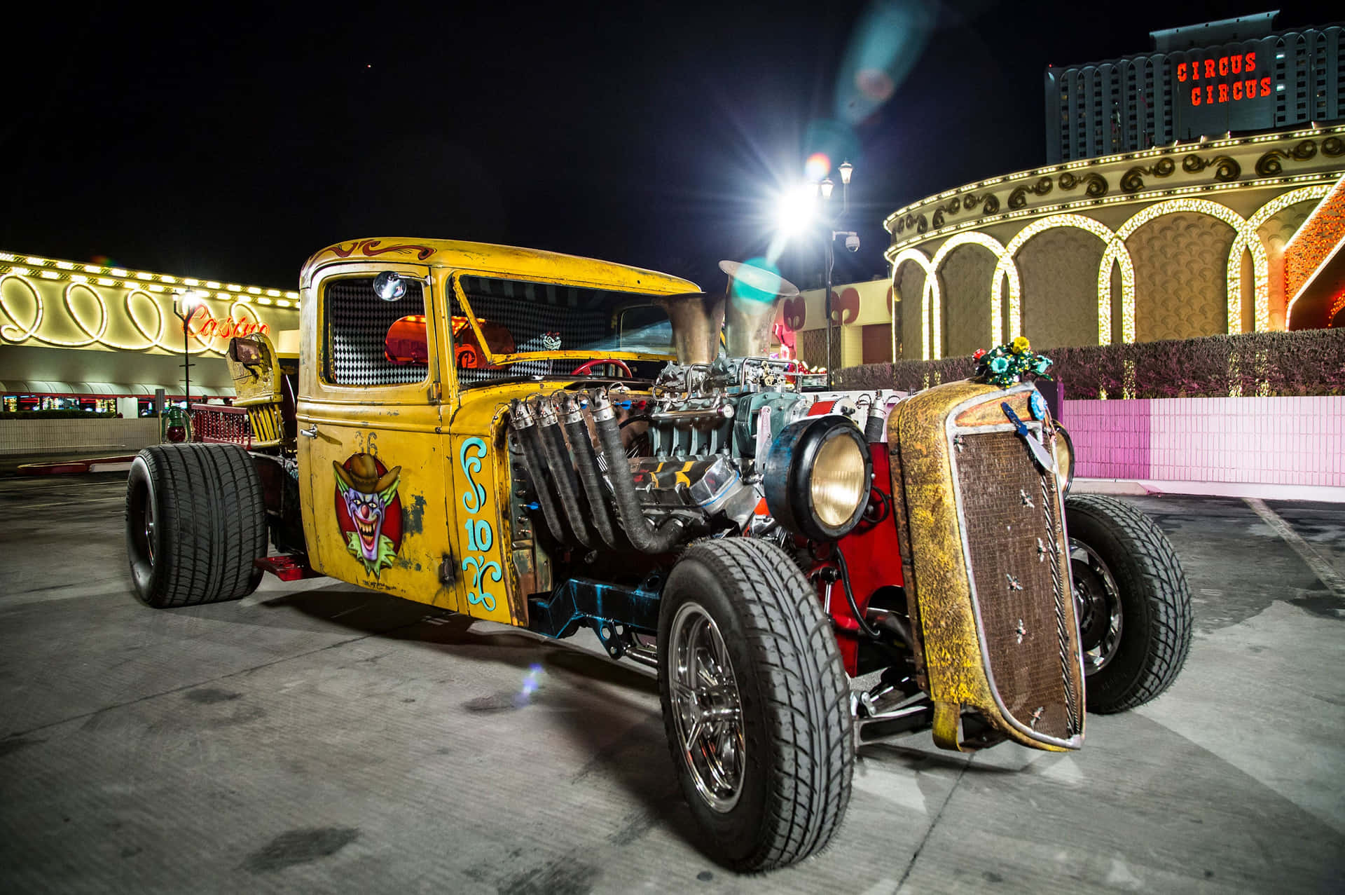  壁紙 — 一輛定製的黃色改裝車，帶有外露引擎和小丑圖案，在夜間於Circus Circus酒店前的霓虹燈下閃閃發光。