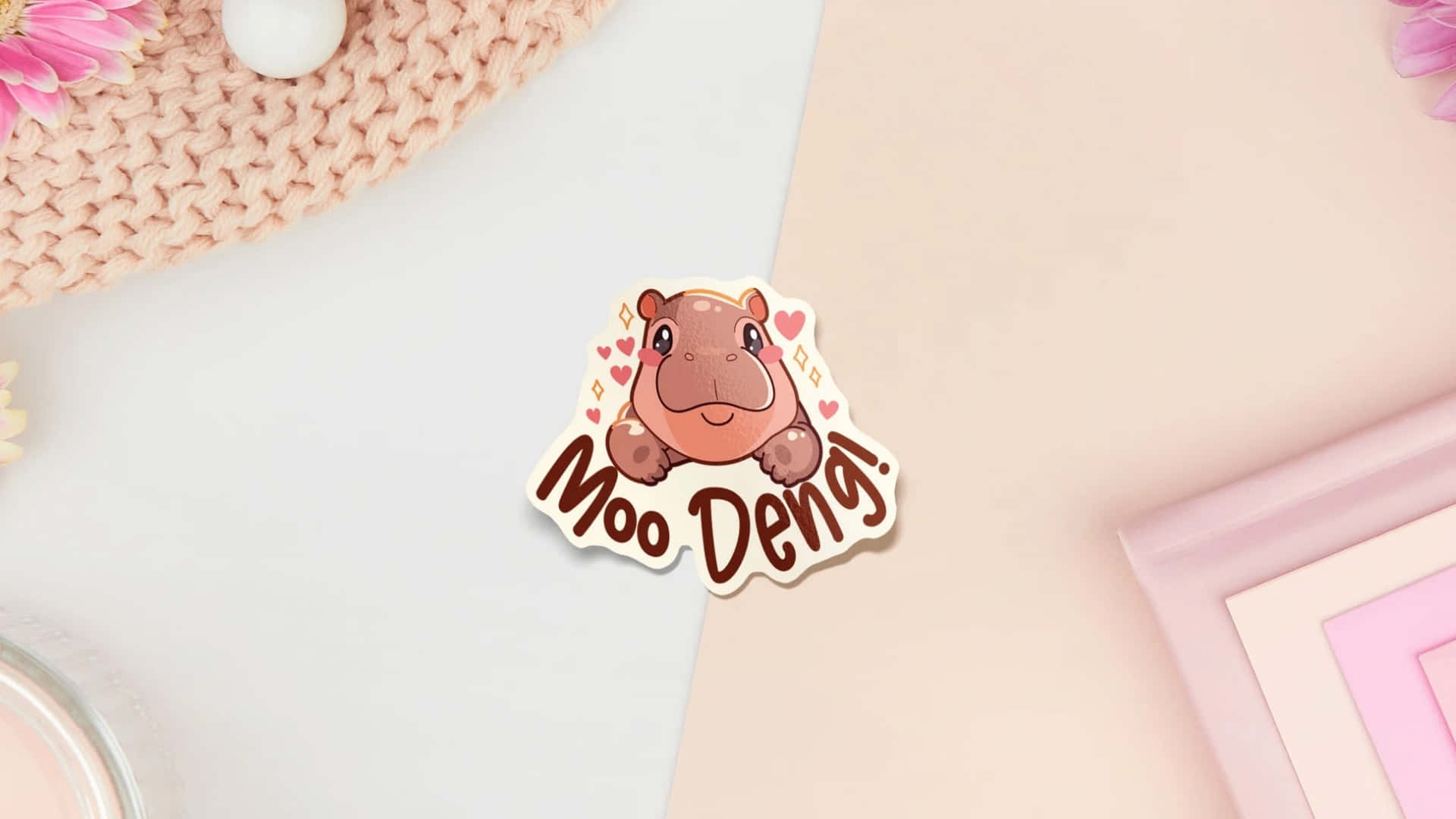  壁紙 — 一個可愛的卡通河馬貼紙，上面有「Moo Deng!」文字，周圍環繞著心形，放在粉彩粉紅色和白色的平鋪佈局上。