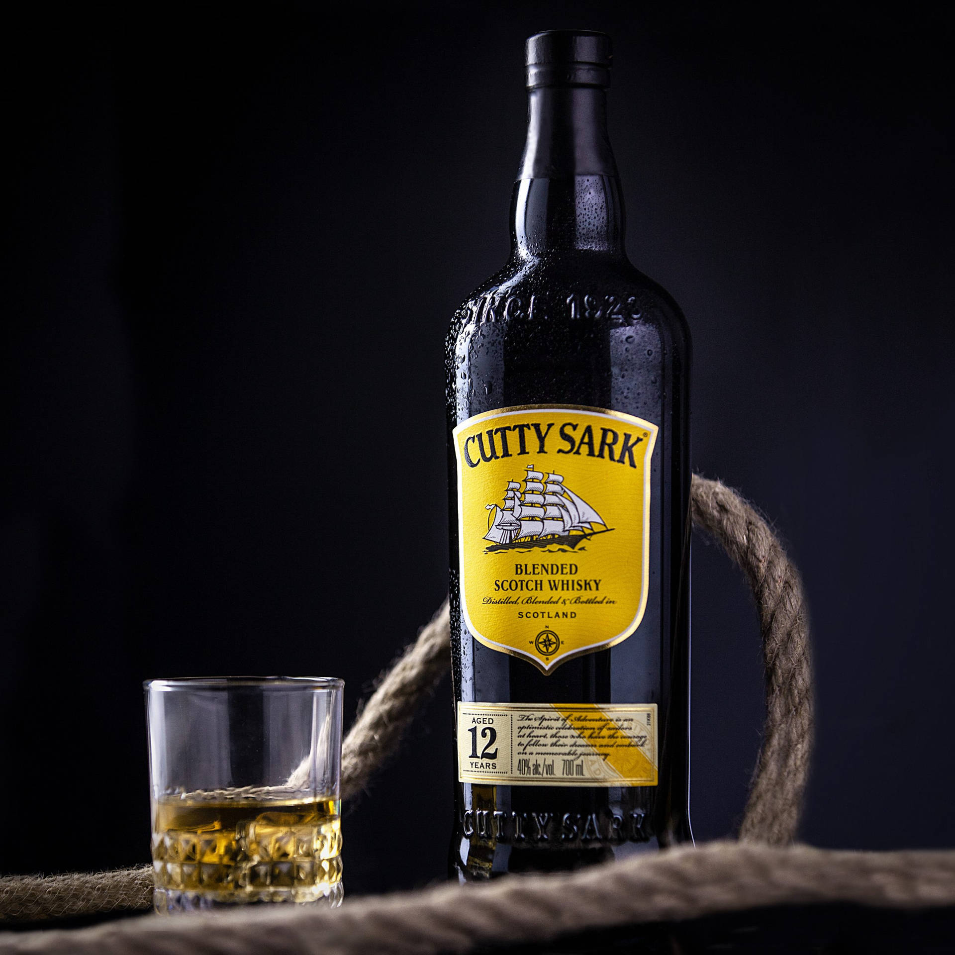 冰鎮Cutty Sark威士忌瓶、玻璃杯和繩索在深色表面上。