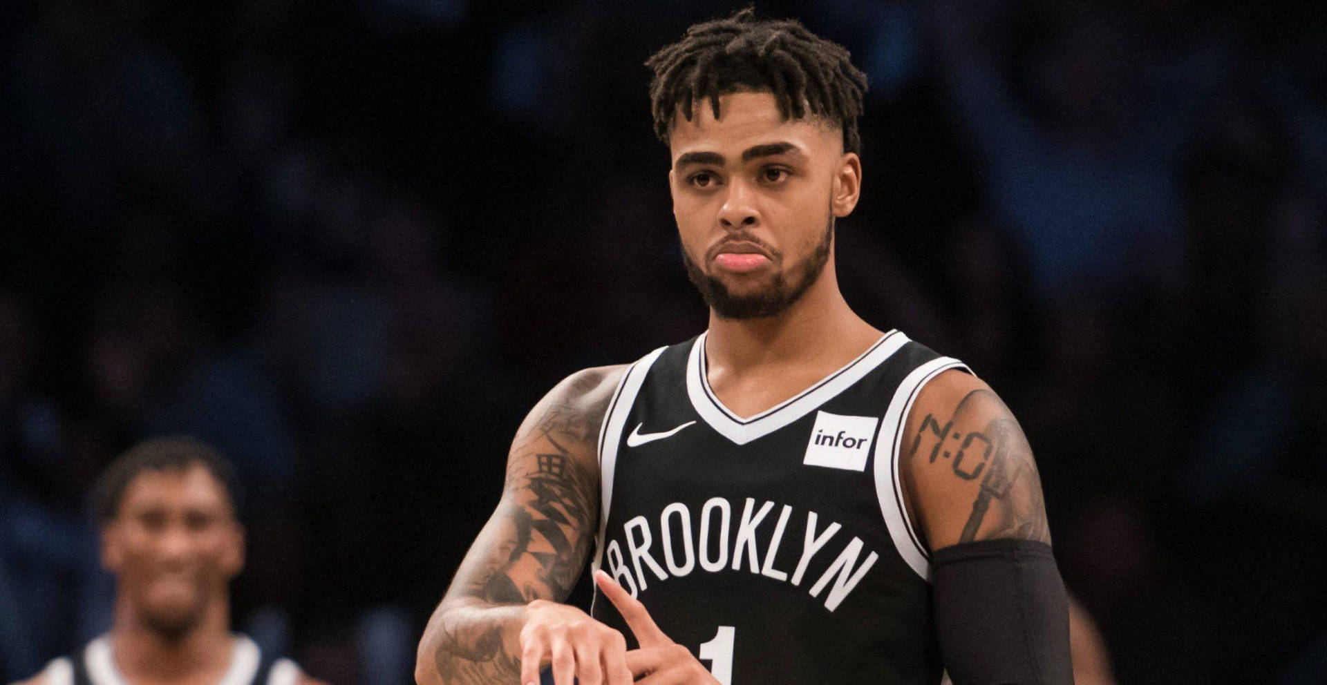 D'Angelo Russell 傷感彎唇 壁紙 — 一位專注的布魯克林籃網籃球運動員，身上有紋身，在比賽中於場館燈光下凝視著。