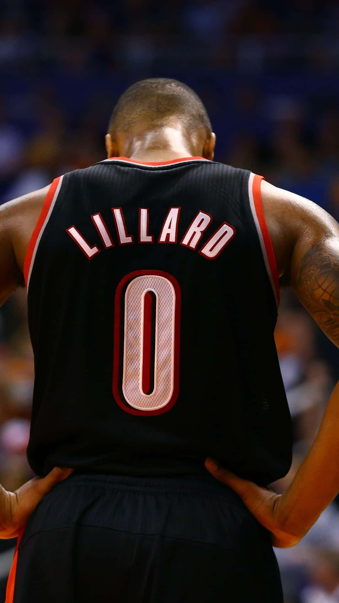 籃球運動員 Damian Lillard 身穿黑色零號球衣，雙手叉腰站在球場上。