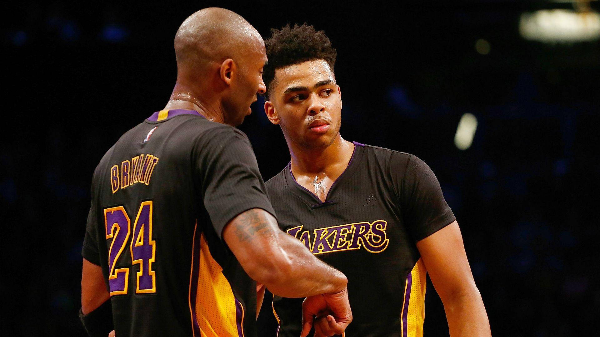 D'Angelo Russell 與 Kobe Bryant 壁紙 — 兩名身穿黑色湖人隊球衣的籃球運動員在場館燈光下進行專注的交談。