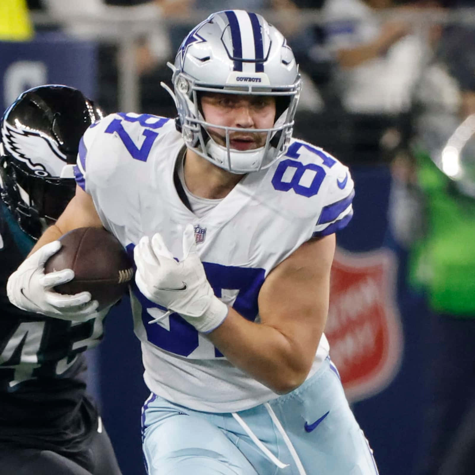  壁紙 — 達拉斯牛仔隊的外接手身穿白色和藍色球衣，在球場上帶著橄欖球奔跑，同時被費城老鷹隊的防守球員追趕。