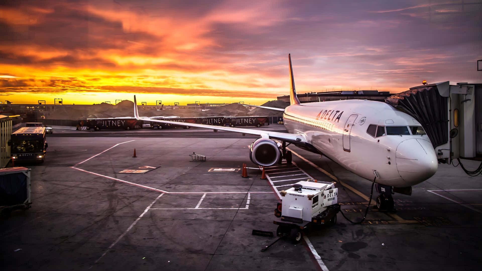  壁紙 — 一架達美航空飛機停在機場閘口，背景是火紅橙紫的日落天空。