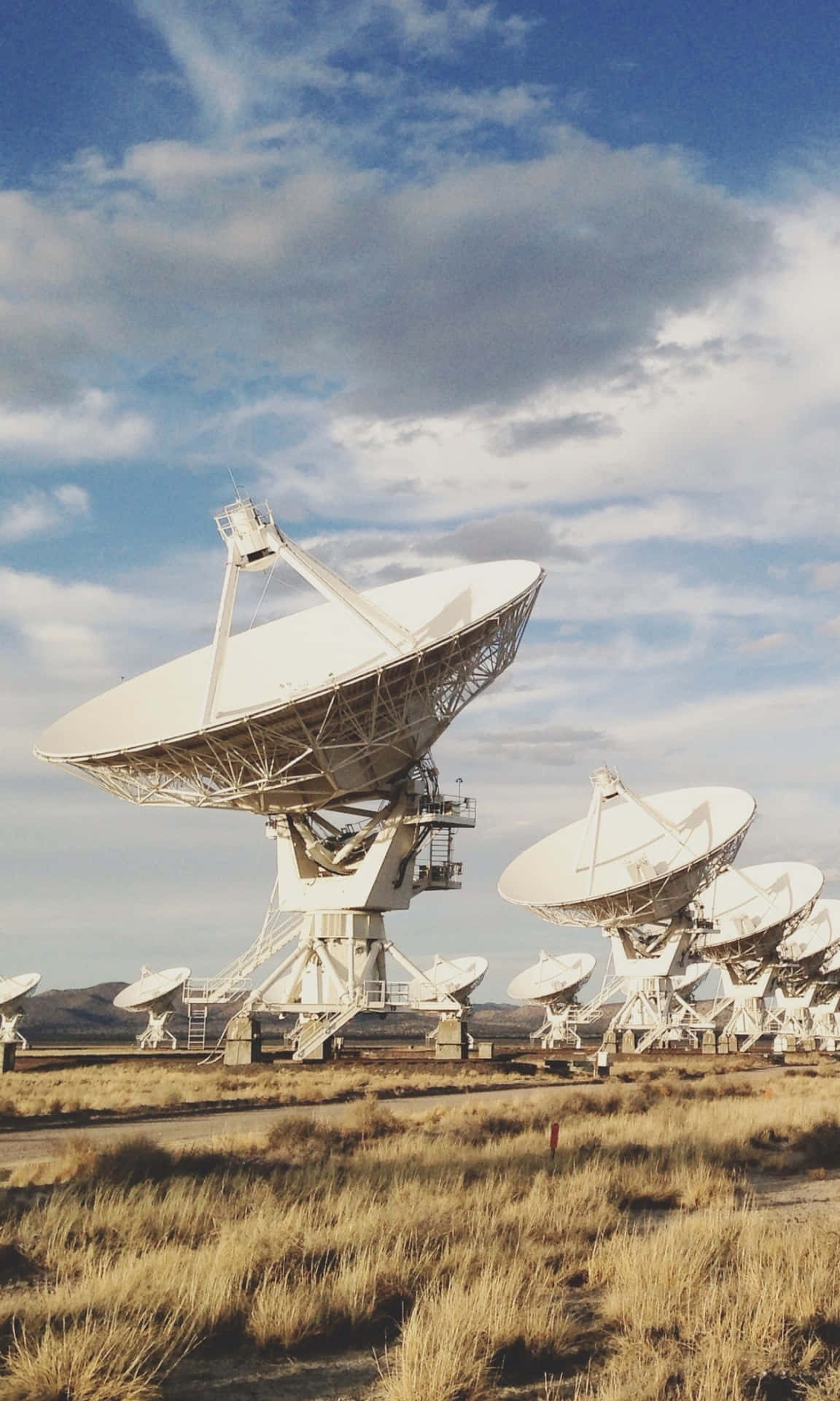  壁紙 — 大型白色衛星天線矗立在乾燥的草地上，天空多雲，藍天白雲。