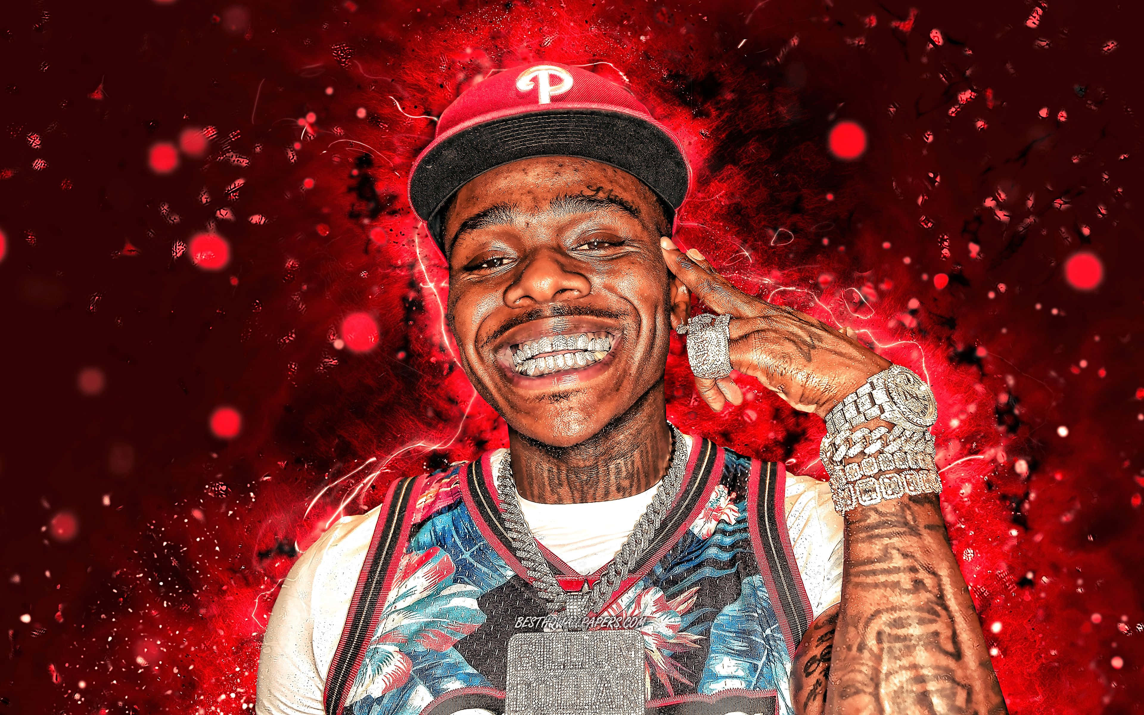 Dababy 在他的元素中 壁紙 — 一個戴紅帽、掛寶石鏈的微笑男子，在充滿電火花的鮮紅色潑濺背景前擺姿勢。