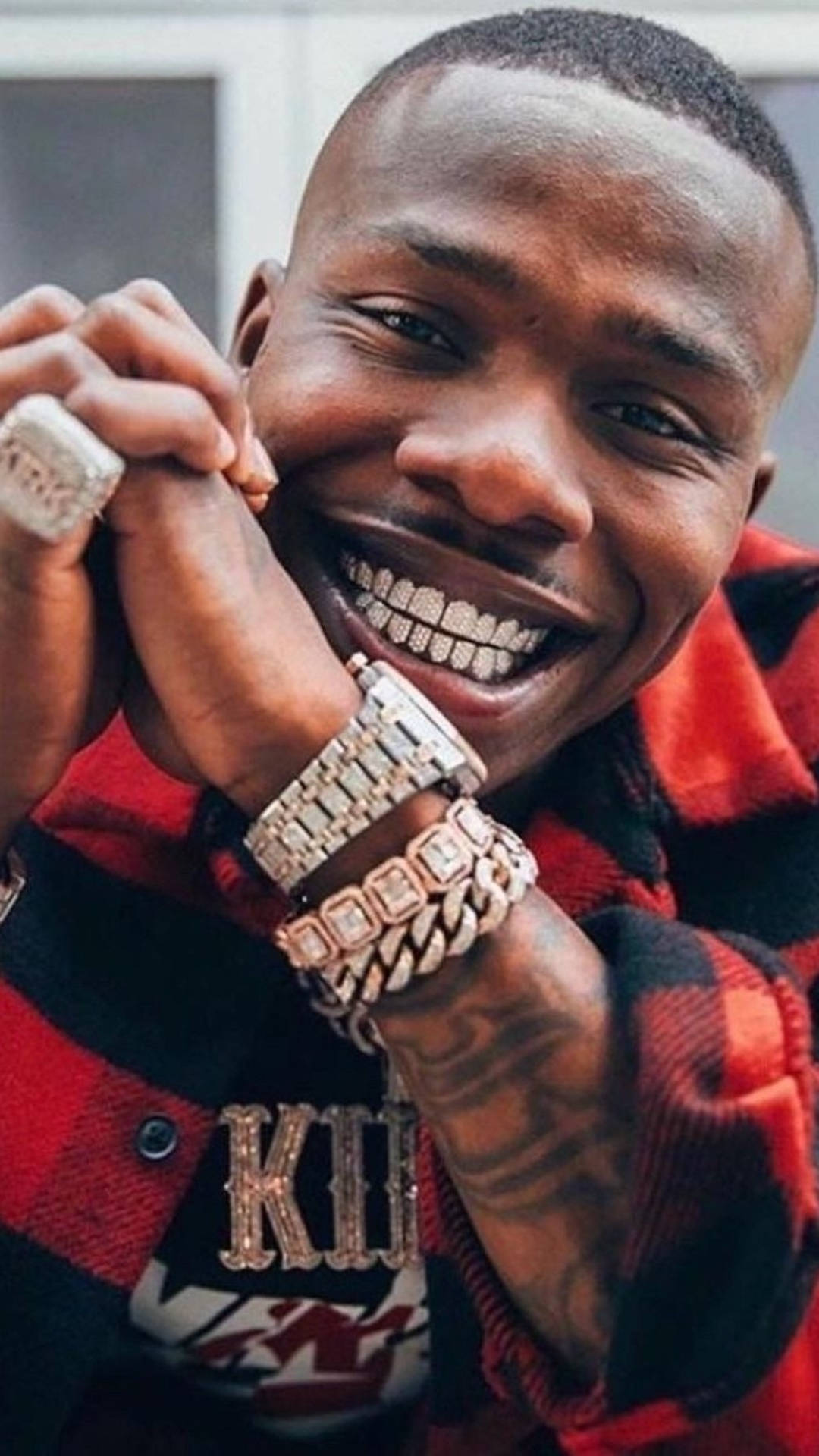 DaBaby 手機搭配奢華配件 壁紙 — 一個微笑的男人穿著紅色格仔襯衫，展示他鑲滿鑽石的牙套和奢華珠寶。