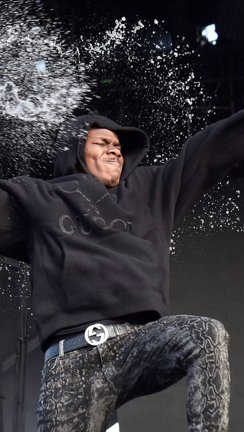 DaBaby 手機開香檳瓶 壁紙 — 一名身穿黑色連帽衫和蛇皮褲的男子在舞台上歡快地跳躍，水花在他周圍戲劇性地飛濺。