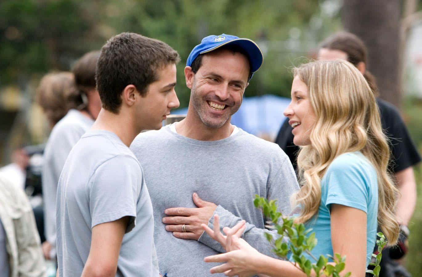 Sarah Roemer 桌布 壁紙 — 一個戴藍色帽子的微笑男子，正與一個年輕男子和一個金髮女子在戶外熱情地笑著交談。