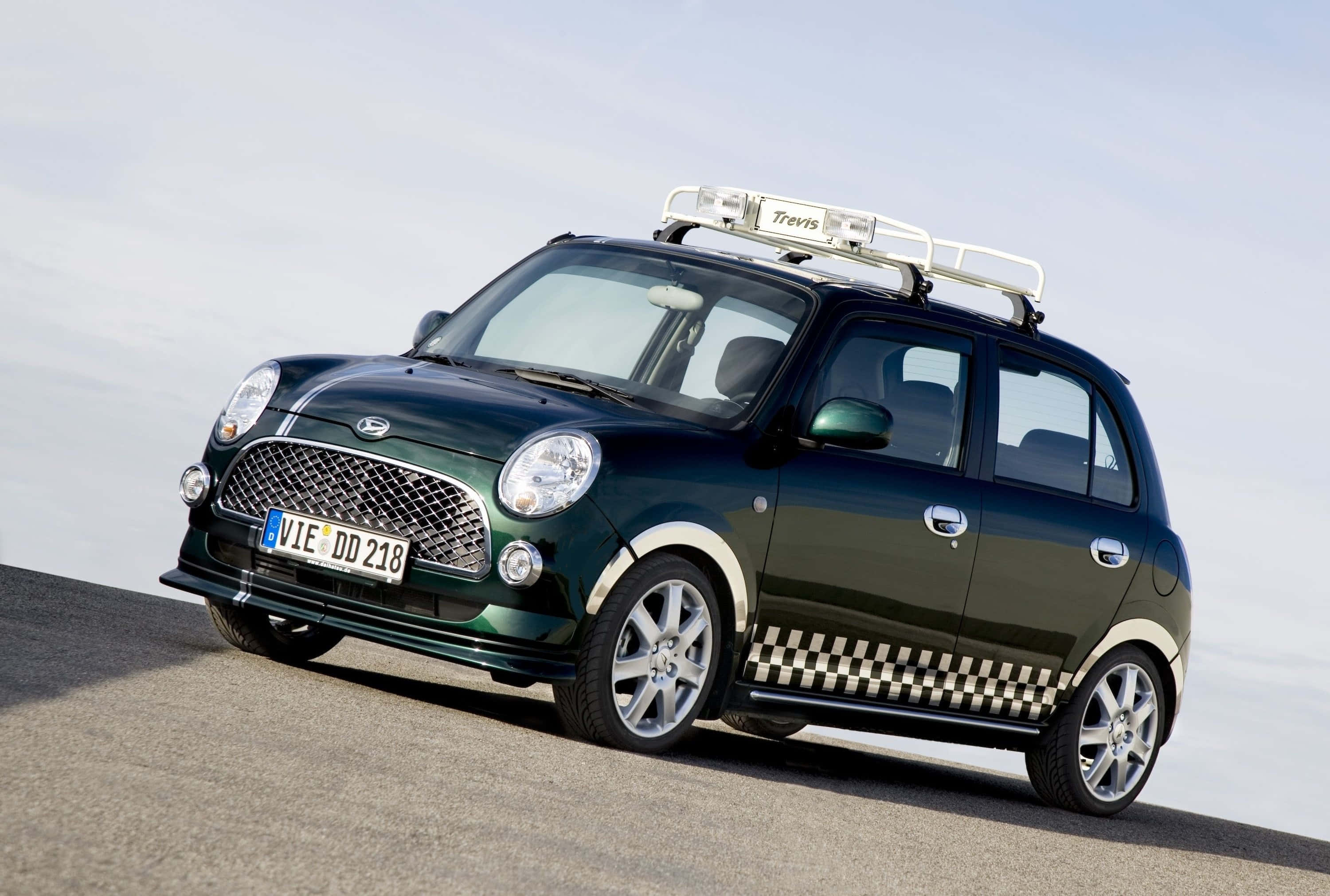型格運動型Daihatsu喺城市環境 壁紙 — 一輛深綠色小型車，帶有格子側條紋和車頂行李架，停在柏油路上，天空蒼白。