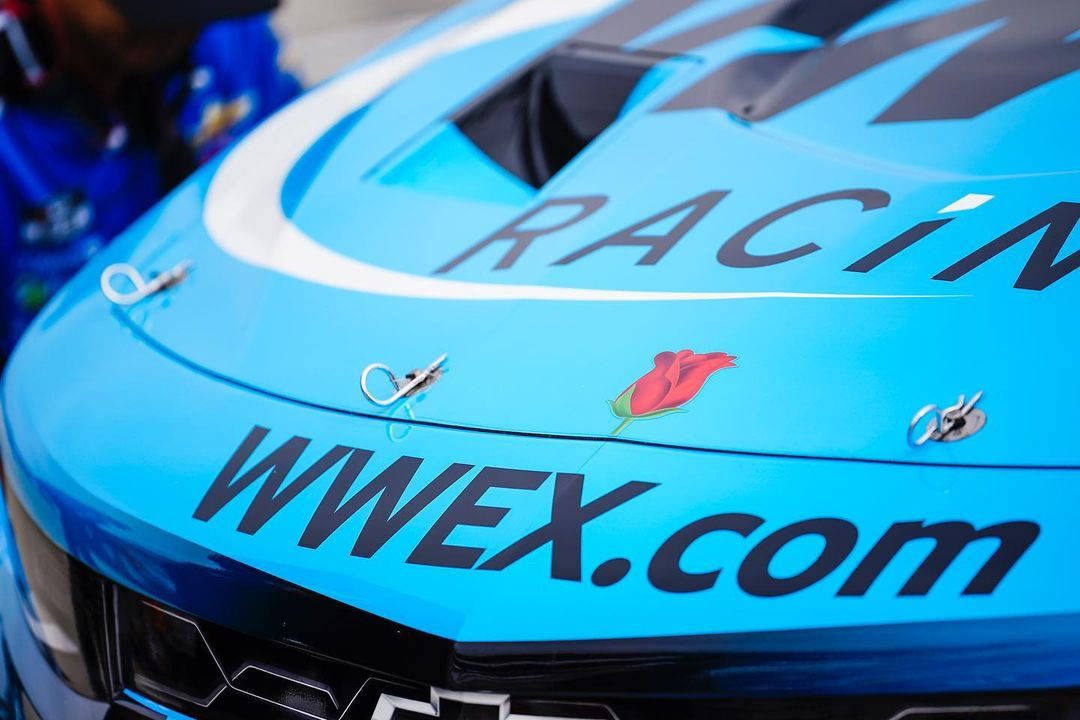 藍色賽車引擎蓋的特寫，上面有 'RACIN' 和 'WWEX.com' 文字以及一個紅色玫瑰貼紙。