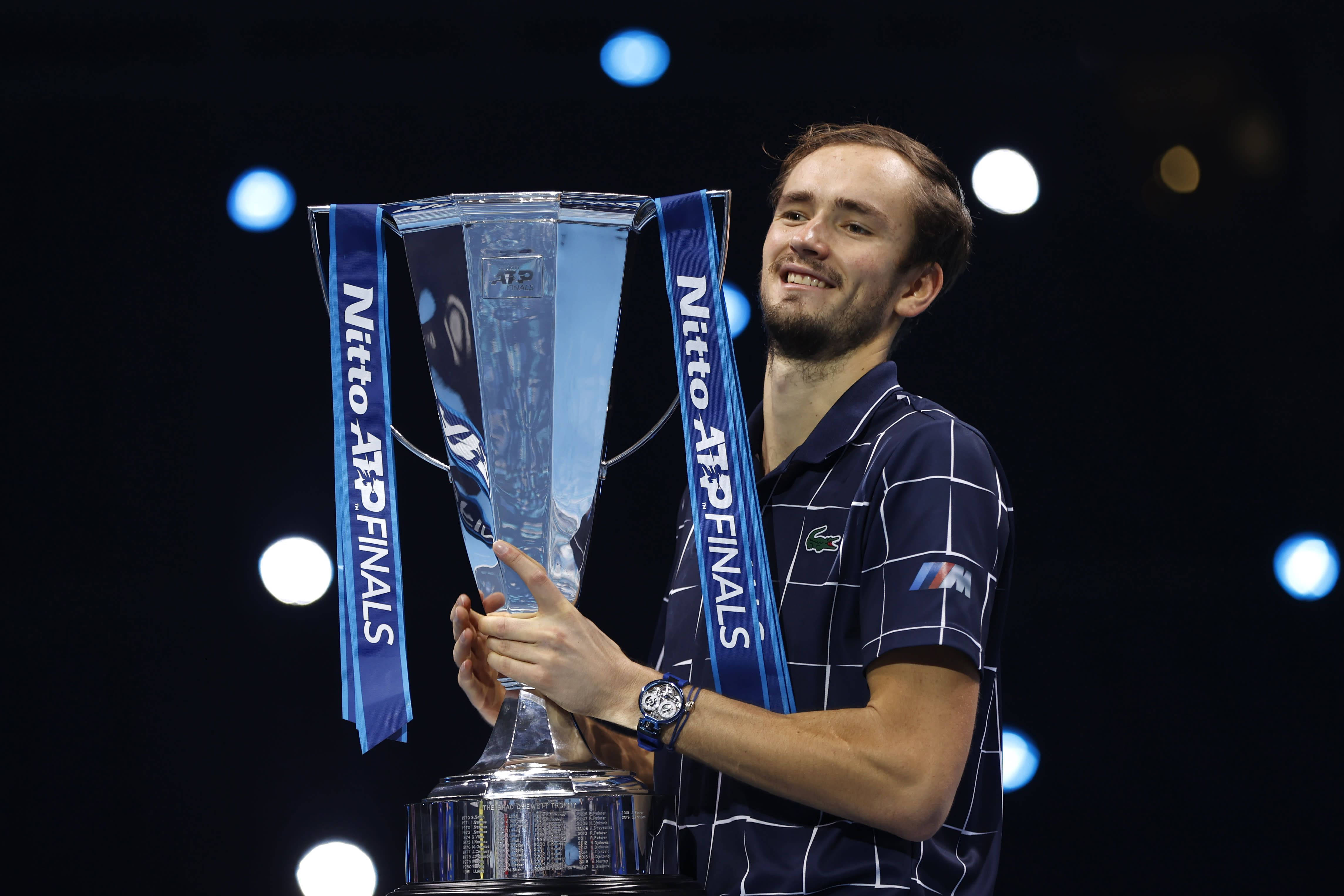 Daniil Medvedev於ATP總決賽奪冠 壁紙 — 一位微笑的網球選手在明亮的舞台燈光下自豪地舉起一個大型玻璃Nitto ATP Finals獎盃。