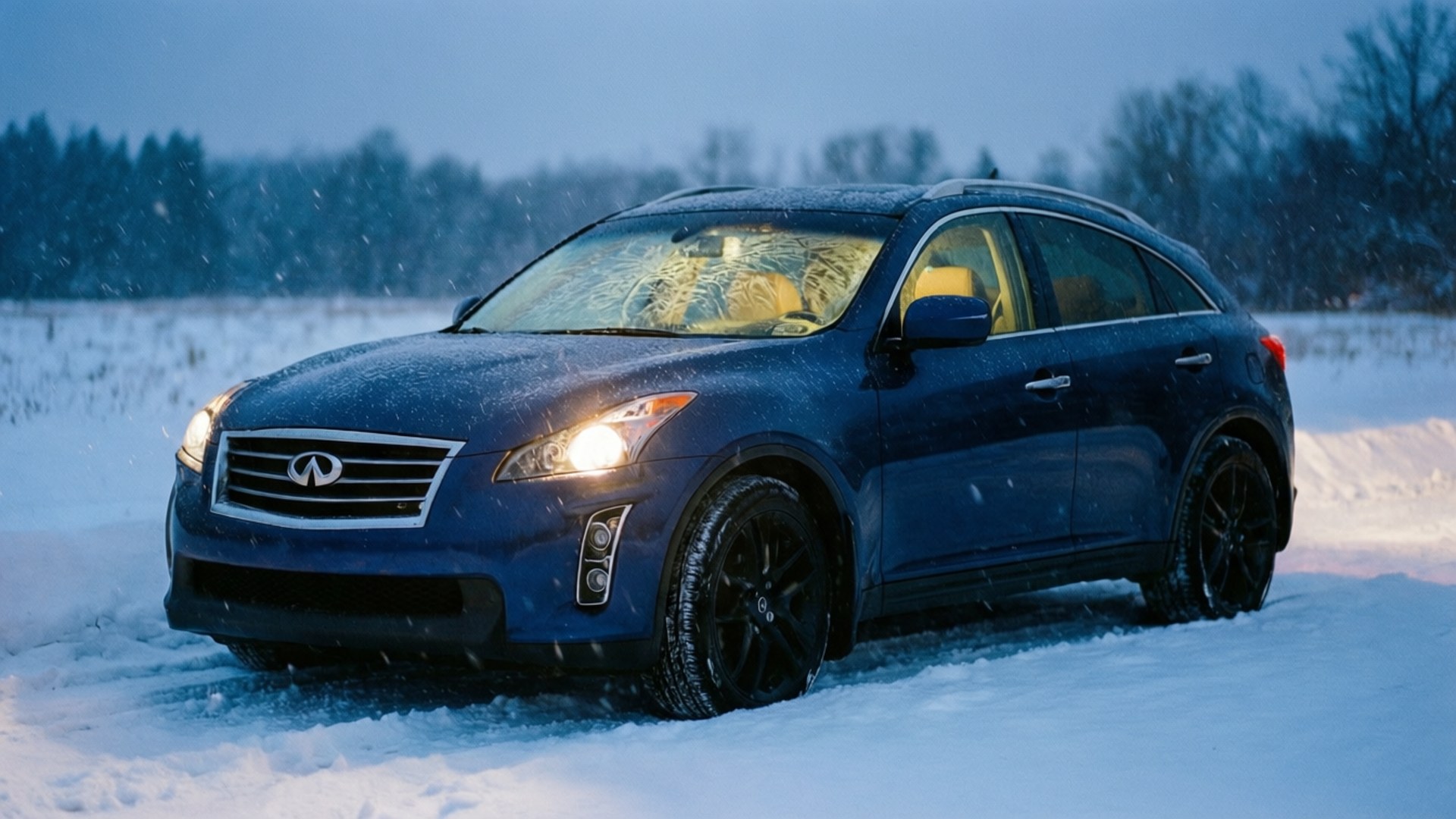 Infiniti Fx35 桌布 壁紙 — 一輛深藍色 Infiniti SUV 在暮色天空下，雪花飄落時，亮著車頭燈駛過雪地。