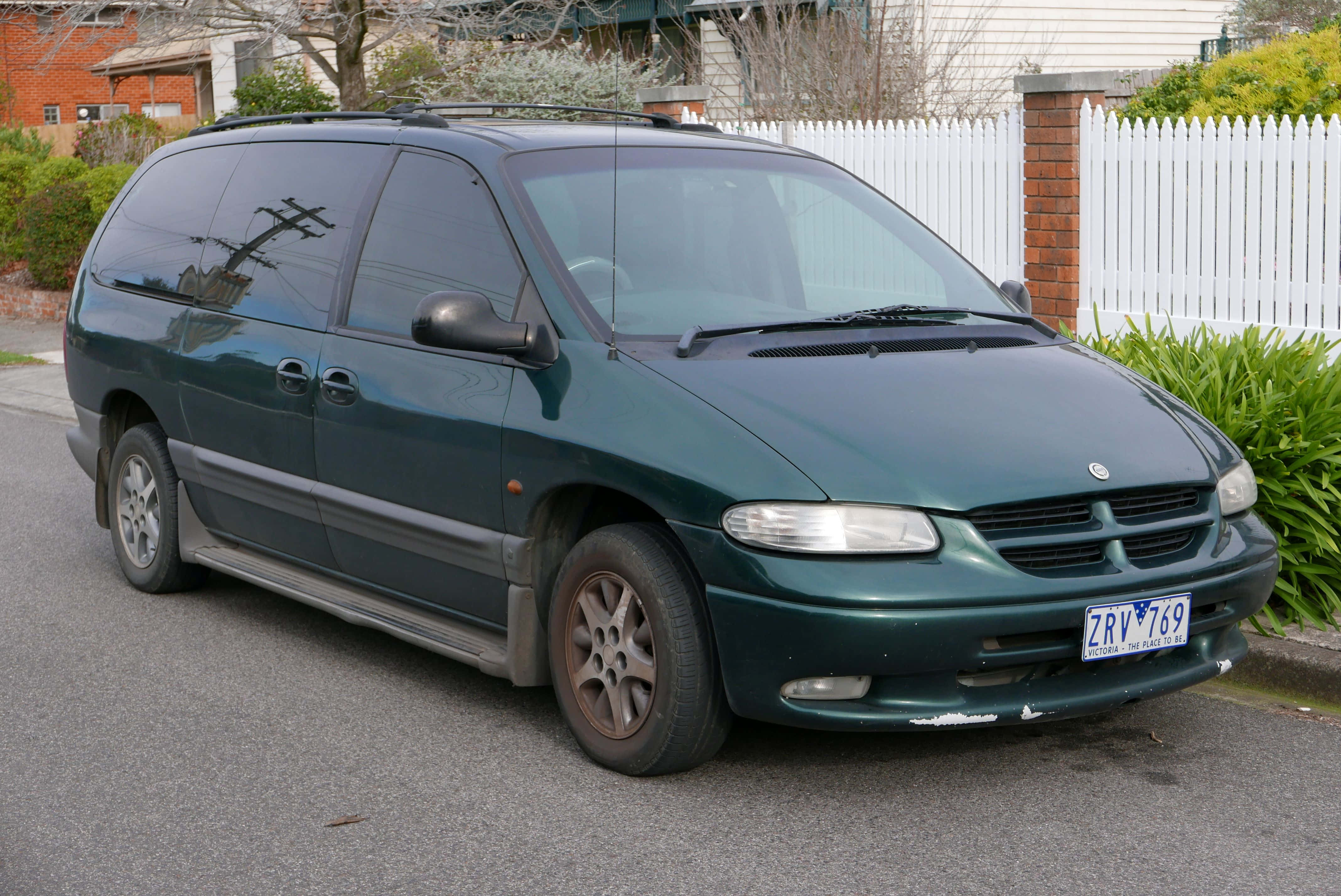 Chrysler Voyager 桌布 壁紙 — 一輛深綠色小型貨車停在郊區街道上，旁邊是白色尖樁籬笆和綠色灌木。