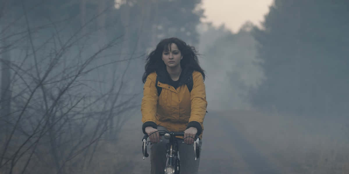 女士在霧氣森林中騎自行車，身穿黃色夾克