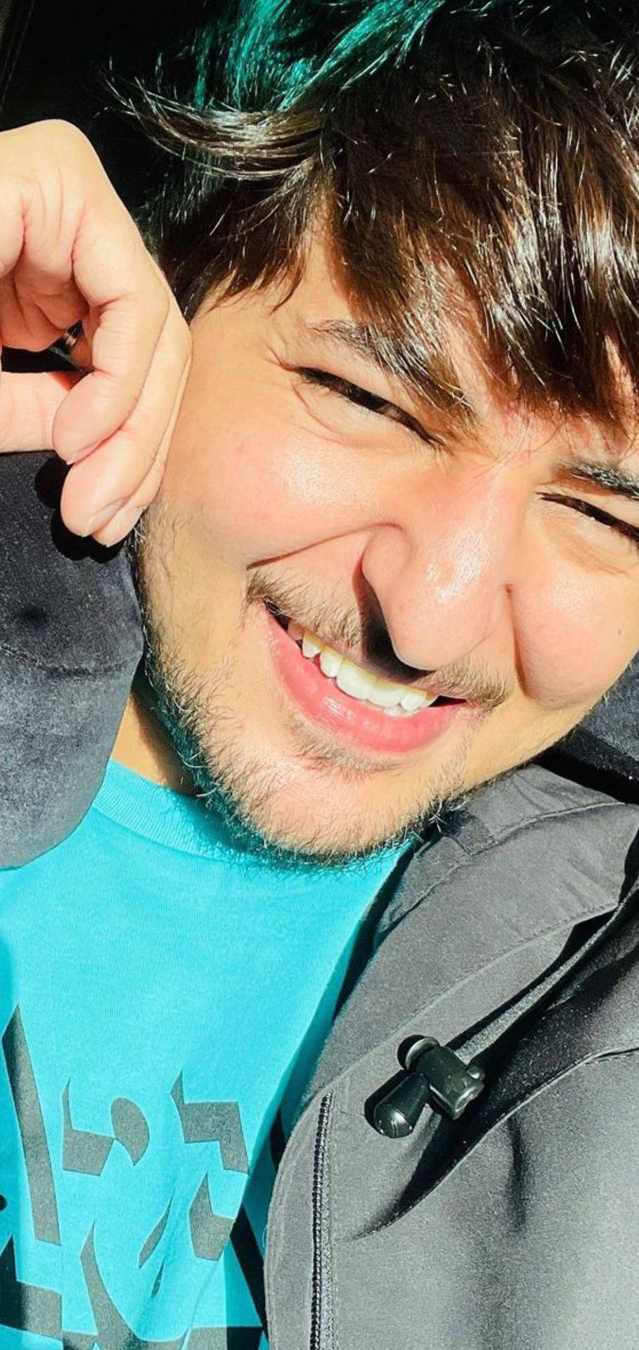 一個有鬍鬚嘅男人喺自拍中燦爛微笑，著住藍色恤衫同灰色外套。