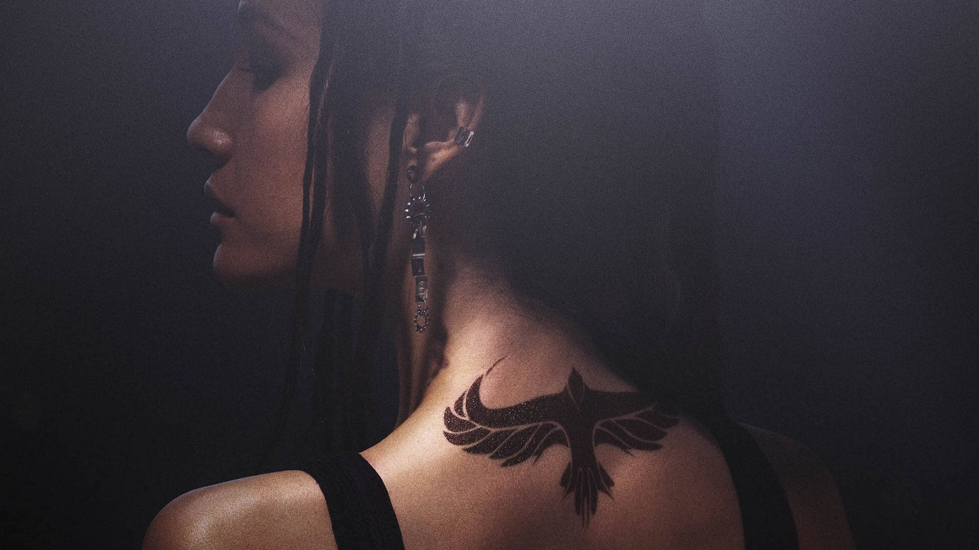 分歧者Dauntless Tori紋身 壁紙 — 一位側面女士在戲劇性燈光下展示她肩上的黑色鳥紋身。
