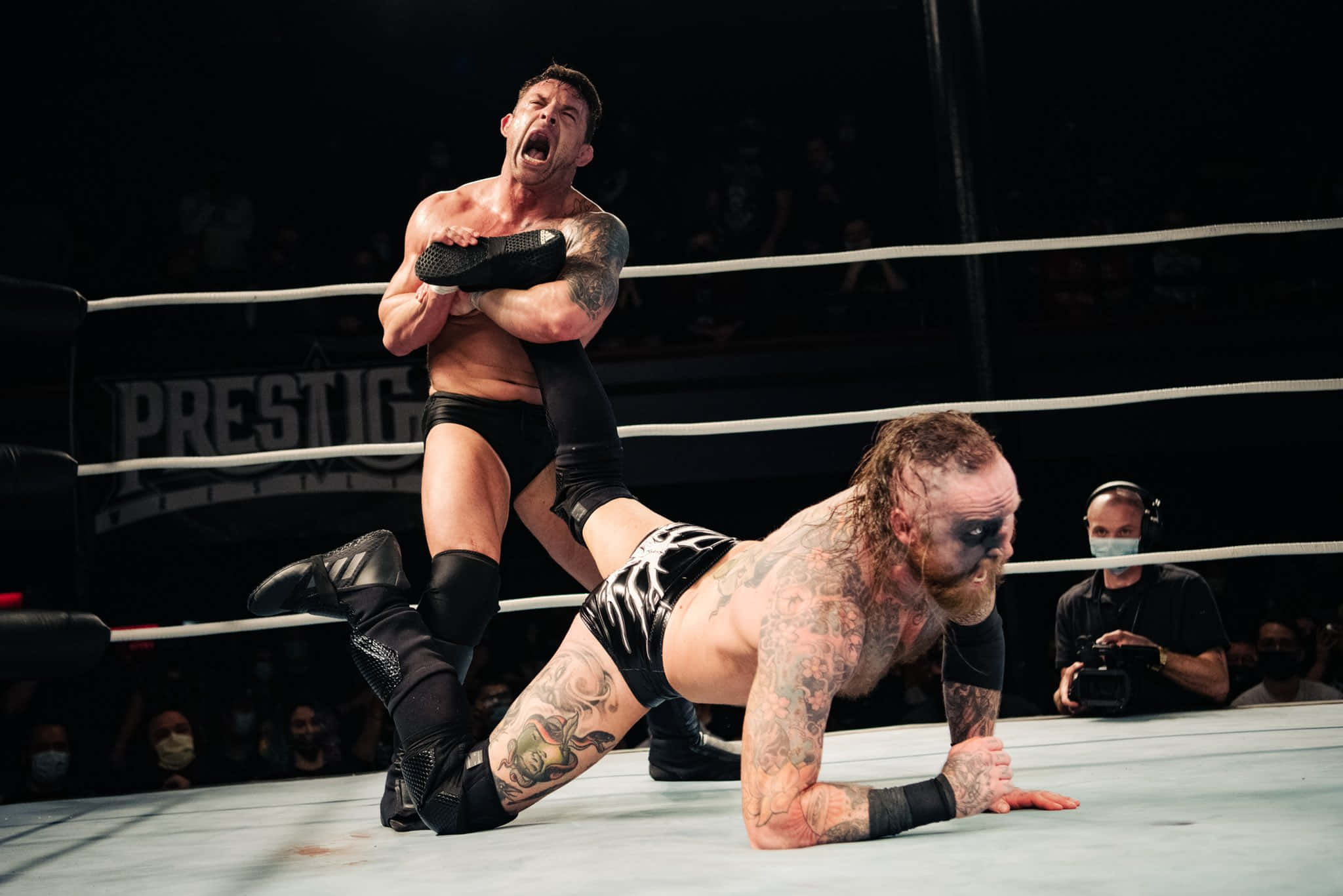 Davey Richards 與 Malakai Black 高張力對決 壁紙 — 兩名紋身摔角手在擂台上，其中一人將另一人舉起，在明亮的場館燈光下做出戲劇性的力量動作。