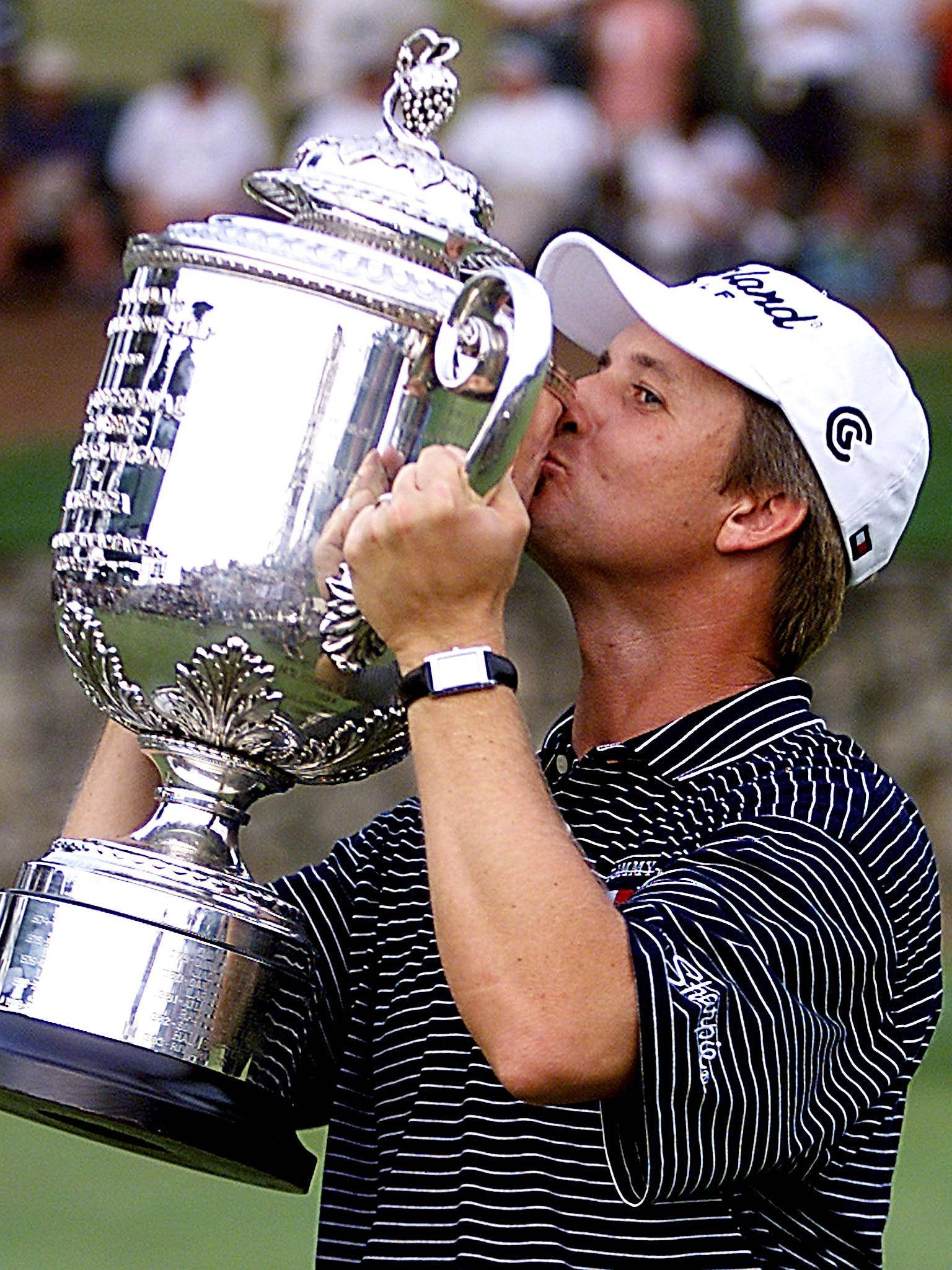 David Toms 親吻獎盃 壁紙 — 一名高爾夫球手戴著白色帽子、穿著條紋襯衫，在綠色球場上親吻一個華麗的大銀色獎盃。