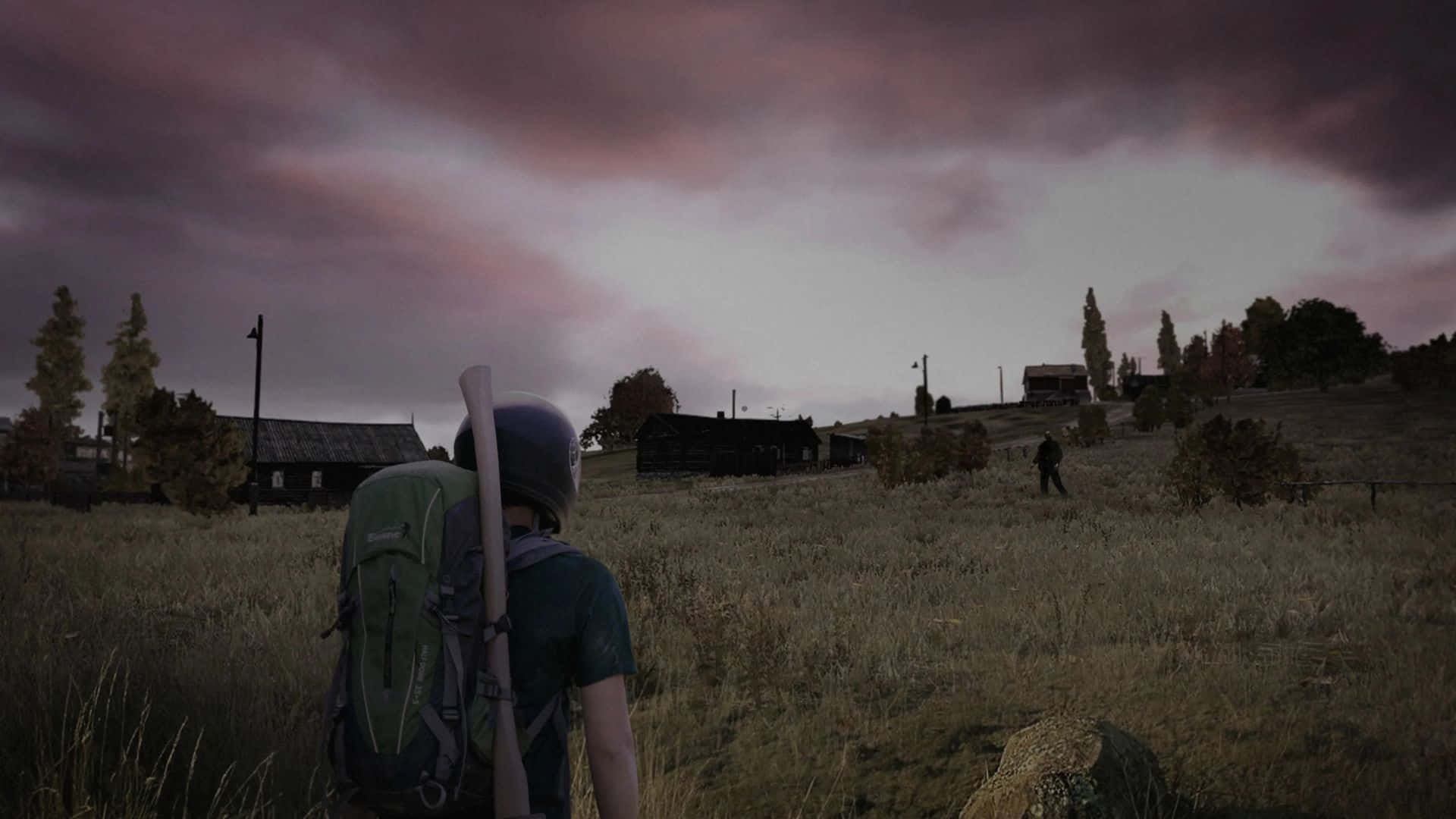DayZ 1080p 背景：男子面對殭屍田地 壁紙 — 一個孤獨的倖存者背著背包、拿著球棒，站在草地上，頭上是風暴前夕的暮色天空，遠處另一個人影在簡陋小屋附近走動。