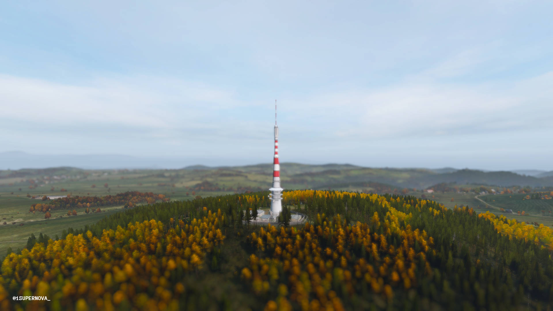 《DayZ》塔頂空拍 壁紙 — 一座高大的紅白條紋塔矗立在森林覆蓋的山丘上，周圍是秋日的樹木，天空柔和湛藍。